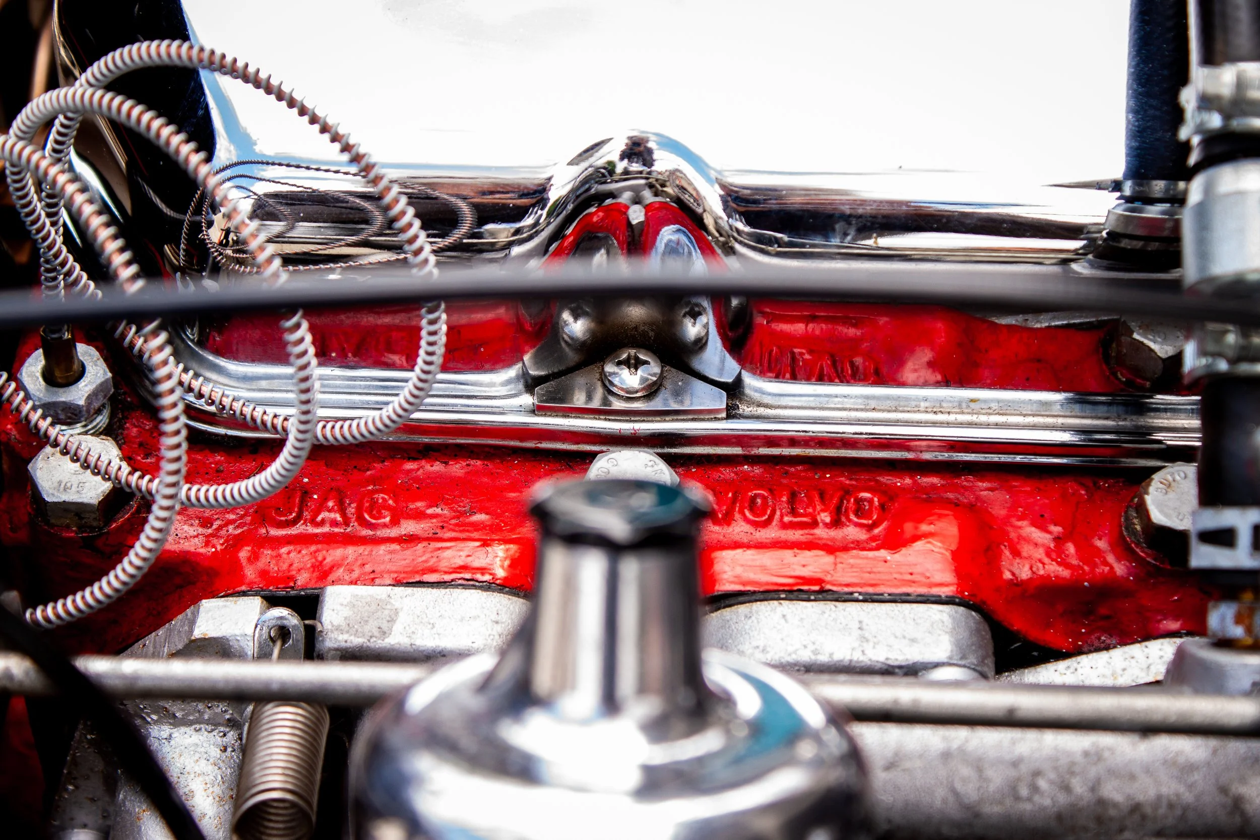 Close-up view of a vintage Jaguar engine with red painted valve cover and various metal components and wiring.