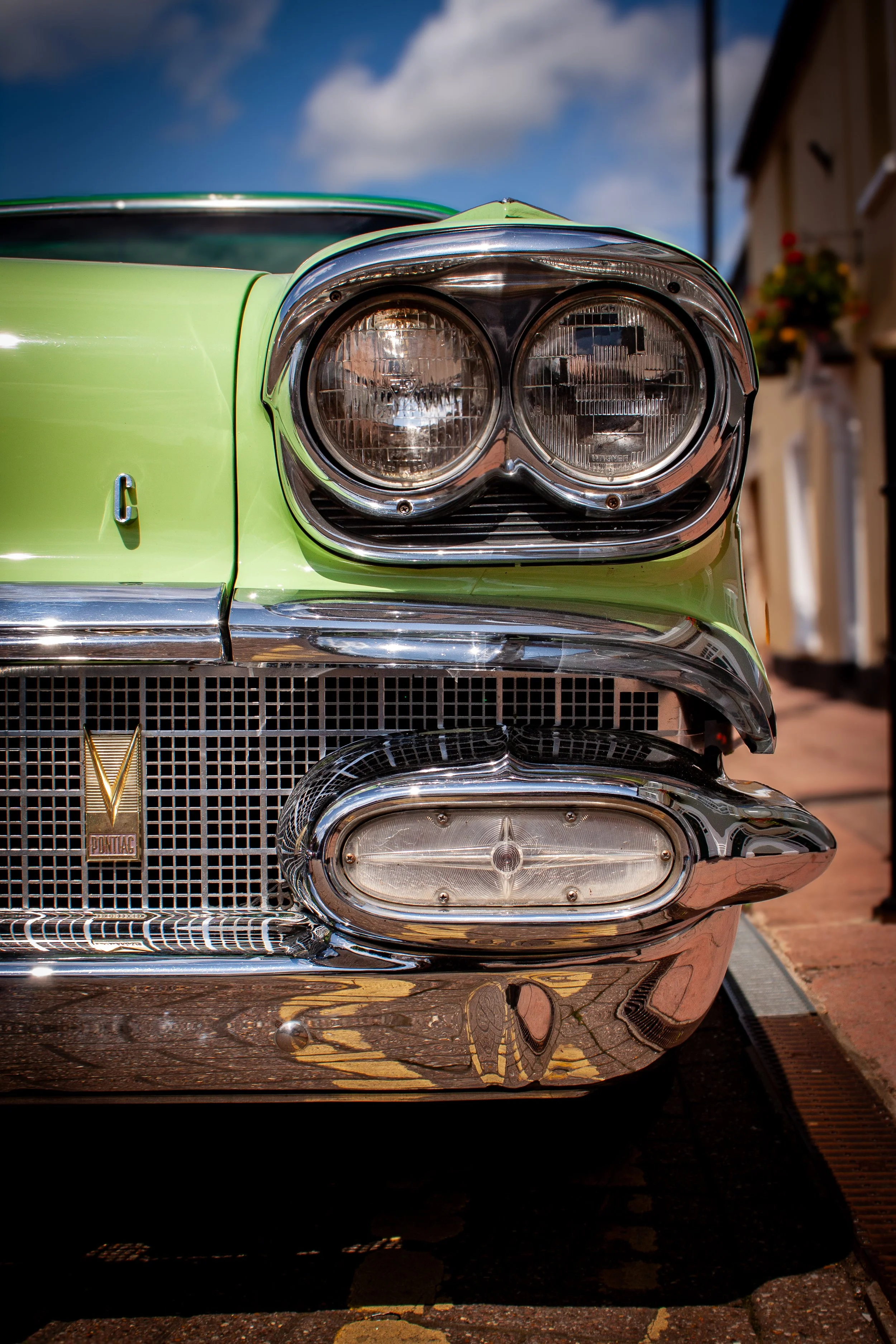 Close-up of the front of a vintage green Pontiac car showing the headlights, grille, and chrome bumper.