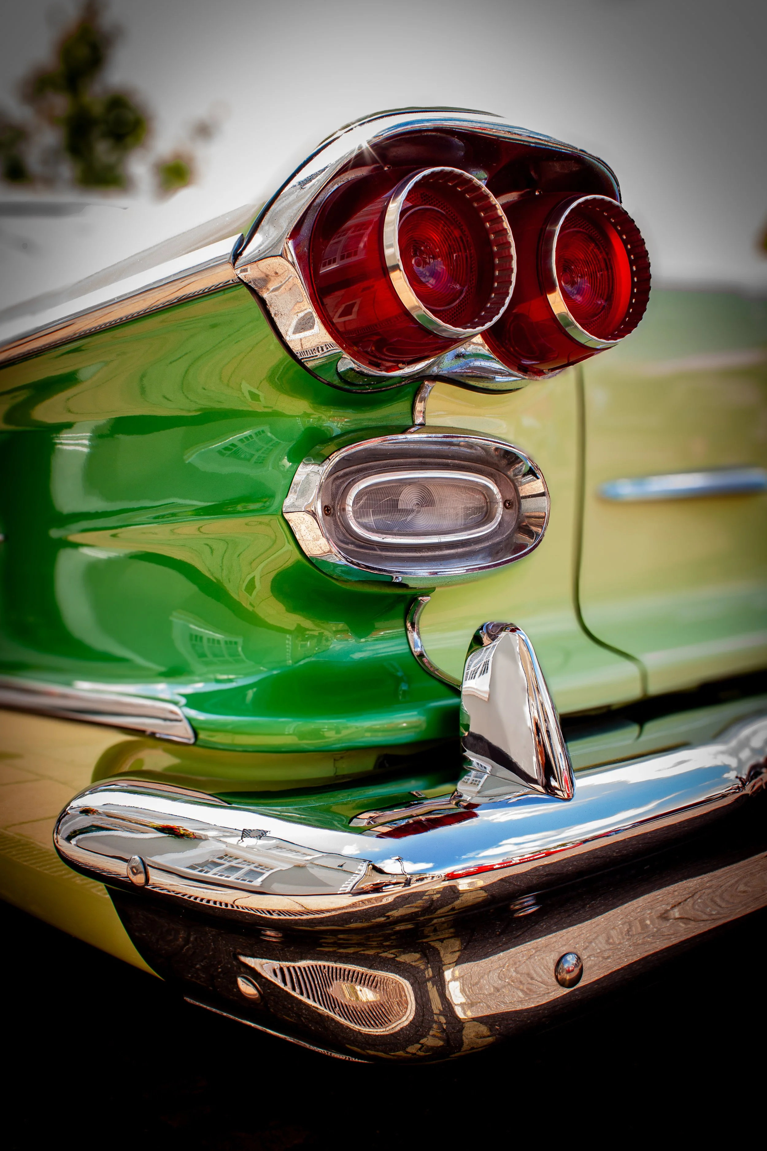 Close-up of the rear of a vintage green car showing red tail lights, a chrome bumper, and decorative trim.