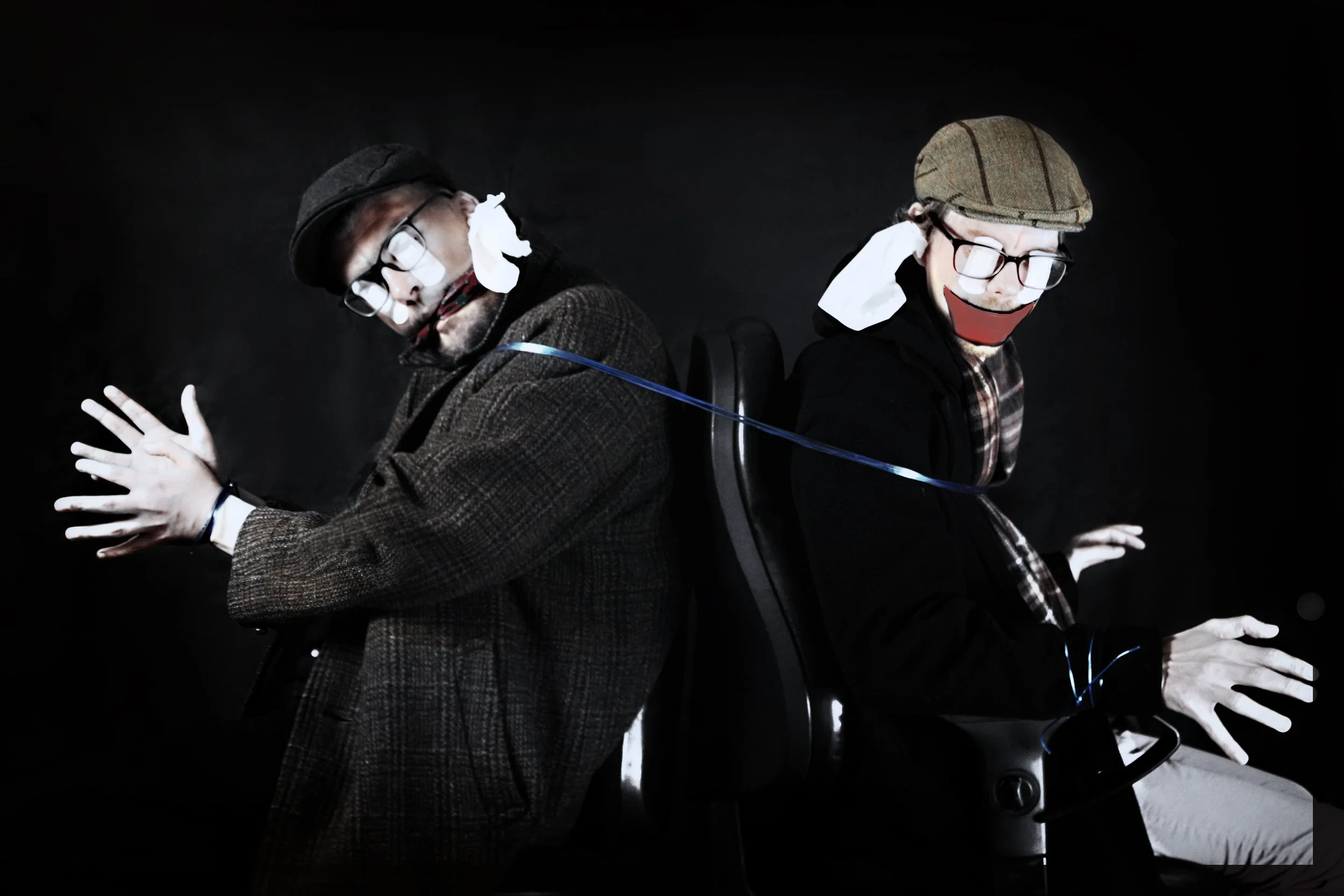 Two people, dressed as puppeteers with white gloves and glasses, are sitting back-to-back, controlling strings connected to each other with a dark background.