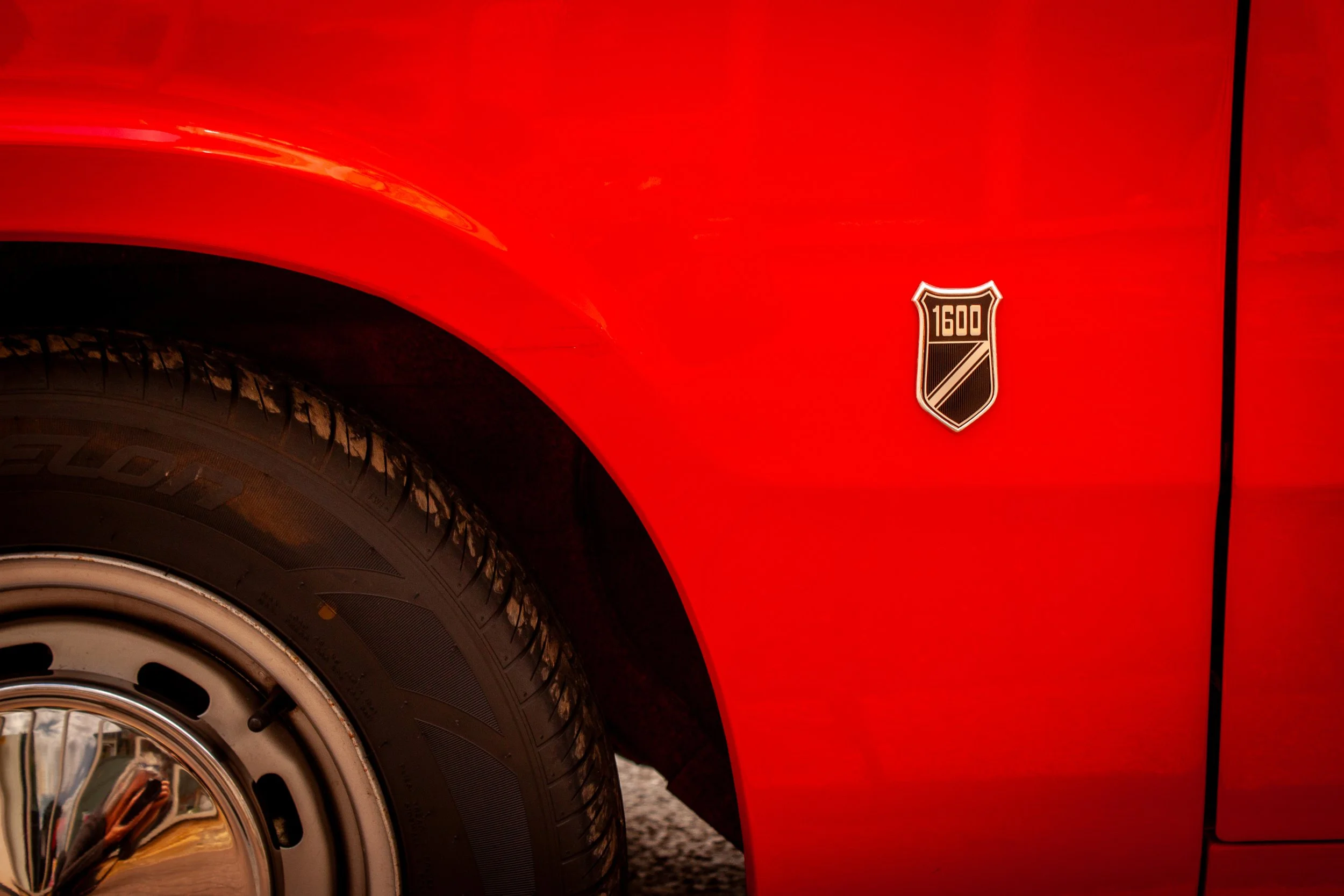 Close-up of a red car's front fender and tire, with a 1600 badge on the side.