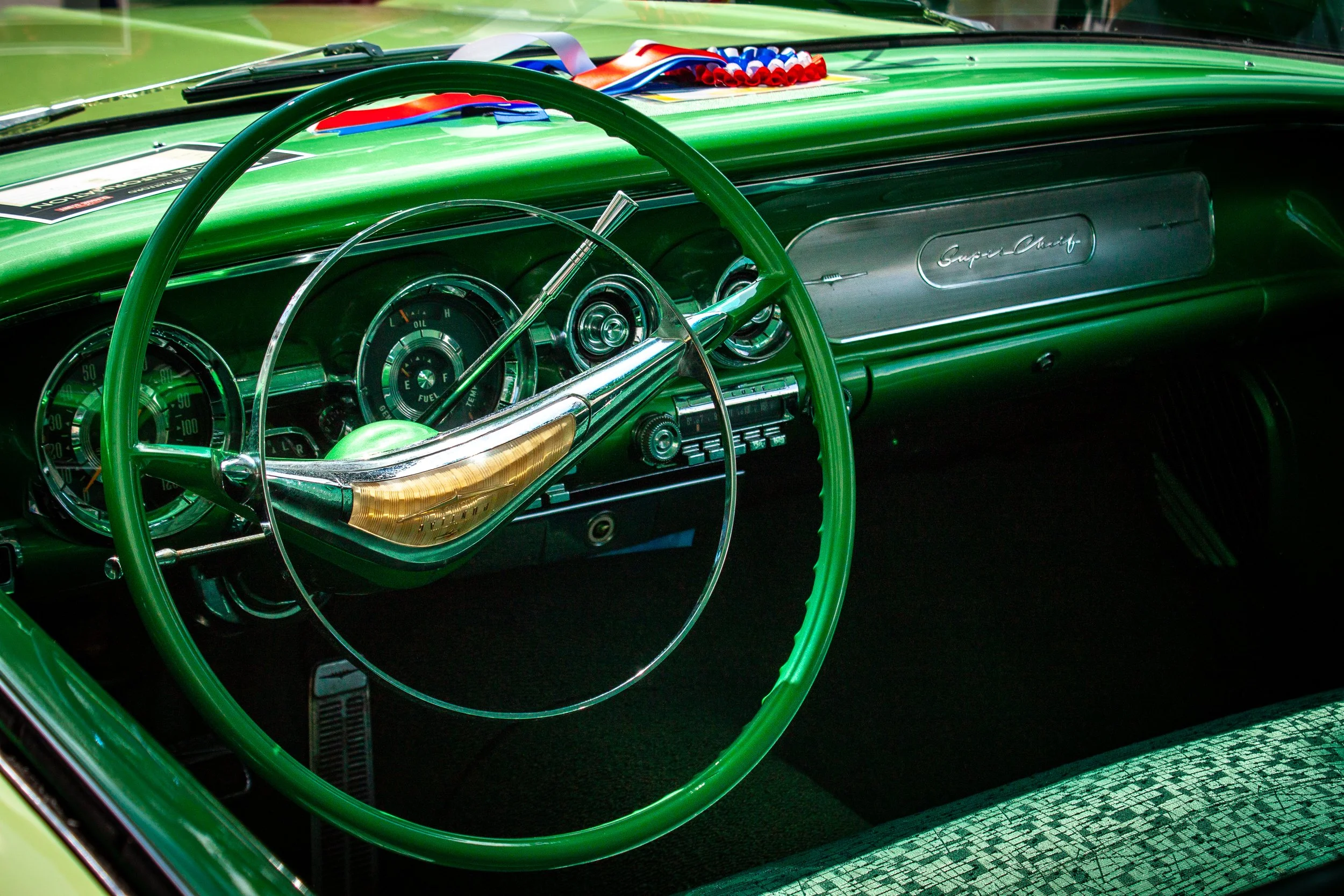 Close-up of the interior dashboard of a vintage green car, featuring a large green steering wheel, retro gauges, and a badge reading Super-Chief.