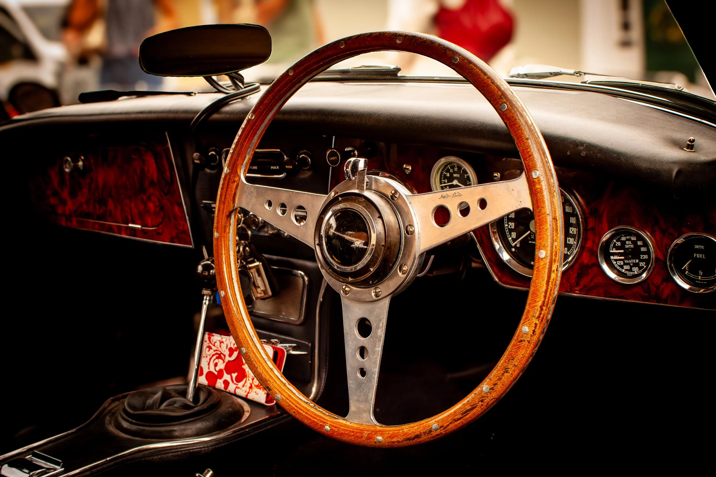Close-up of a vintage car dashboard showing a wooden steering wheel, a speedometer, fuel gauge, and other analog gauges.