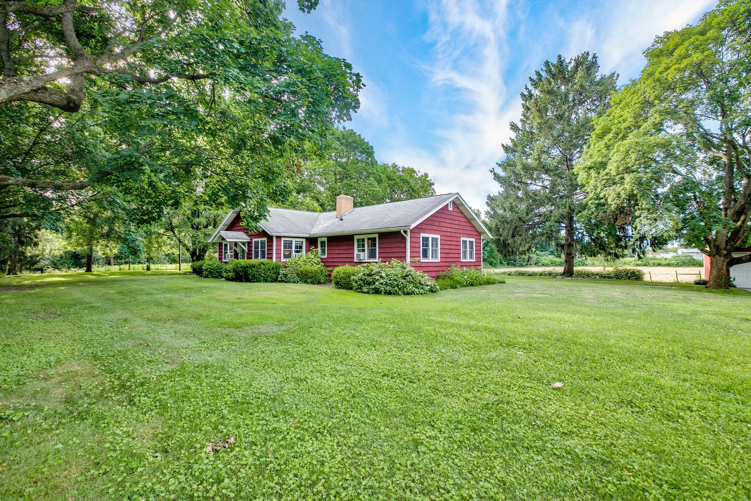 Red farmhouse at KINTZ Farm surrounded by green lawn and trees in a peaceful countryside setting in Indiana