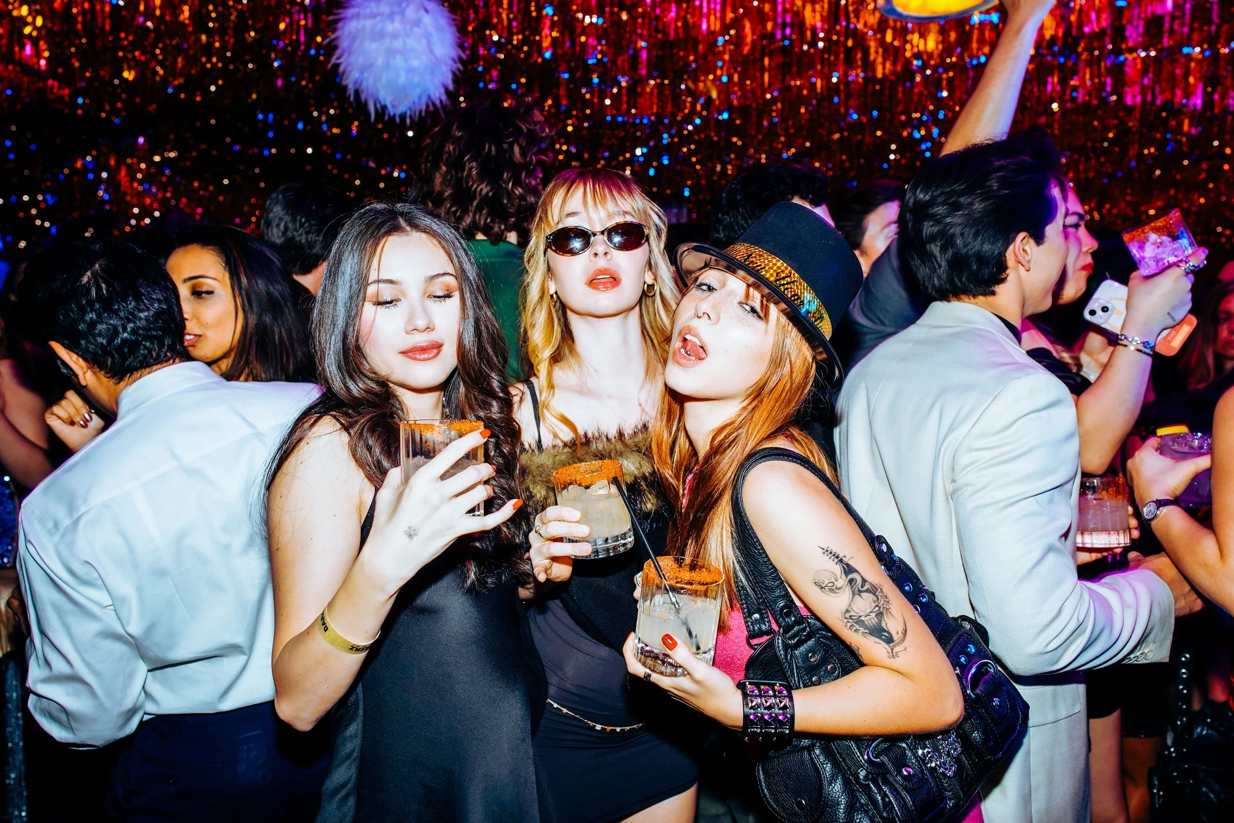 People at a lively party with colorful lighting, holding drinks, and enjoying themselves.