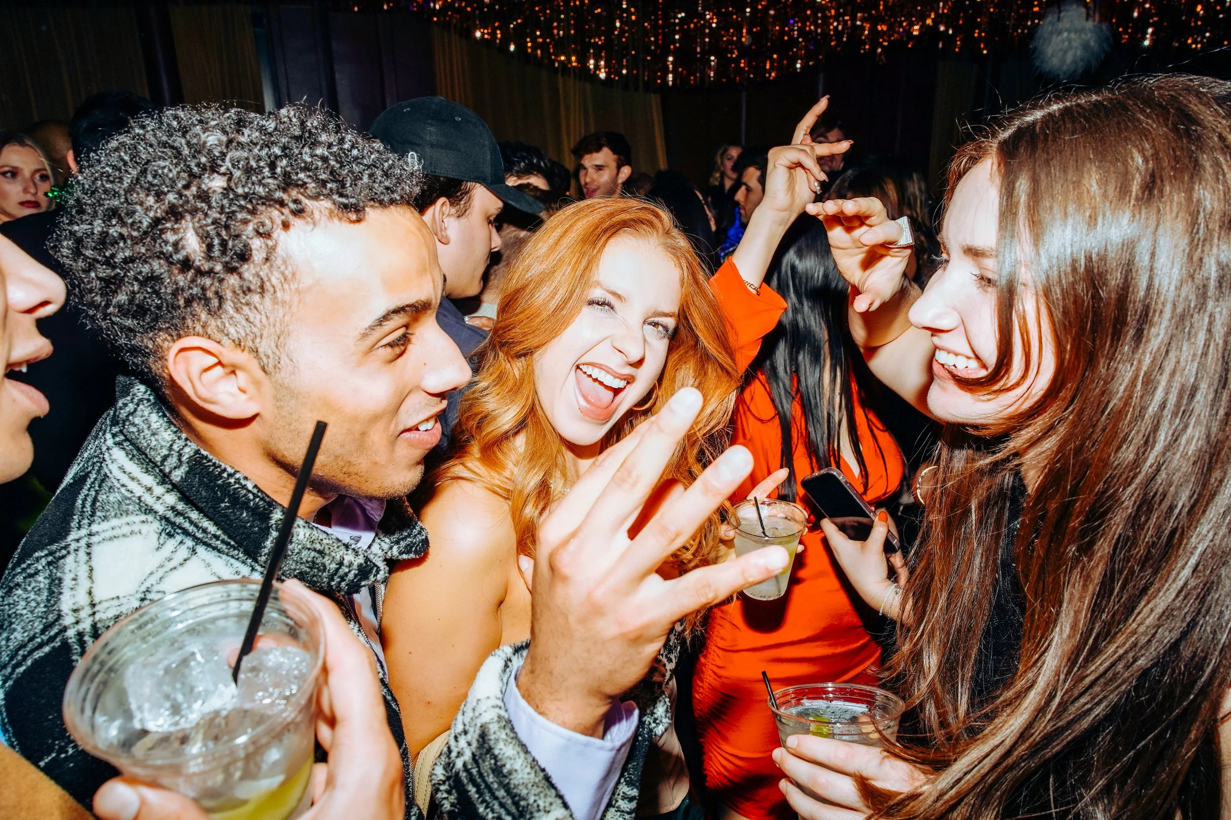 Group of young adults at a lively party, dancing, holding drinks, and having fun.