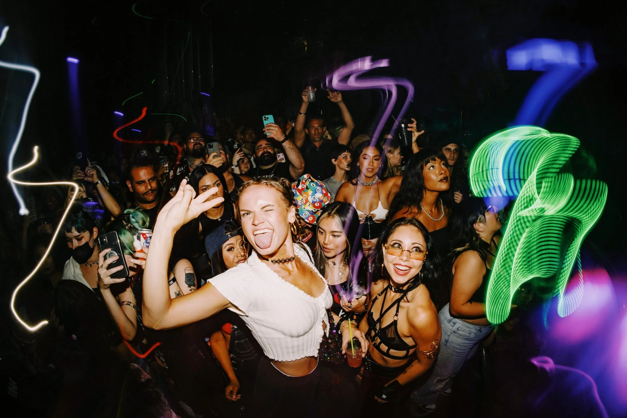 Young people dancing and smiling at a nightclub, with colorful light streaks and neon lighting.