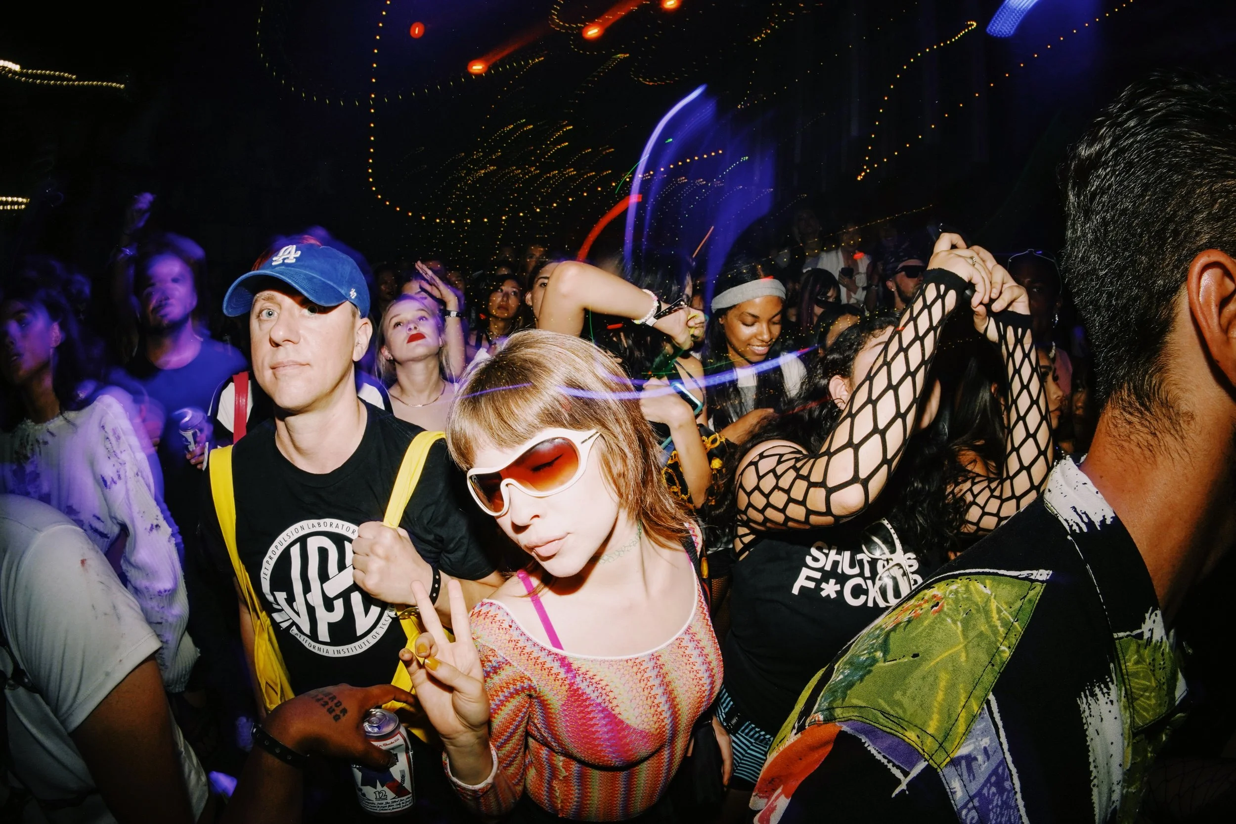 People dancing at a crowded nightclub with colorful lights and laser effects.