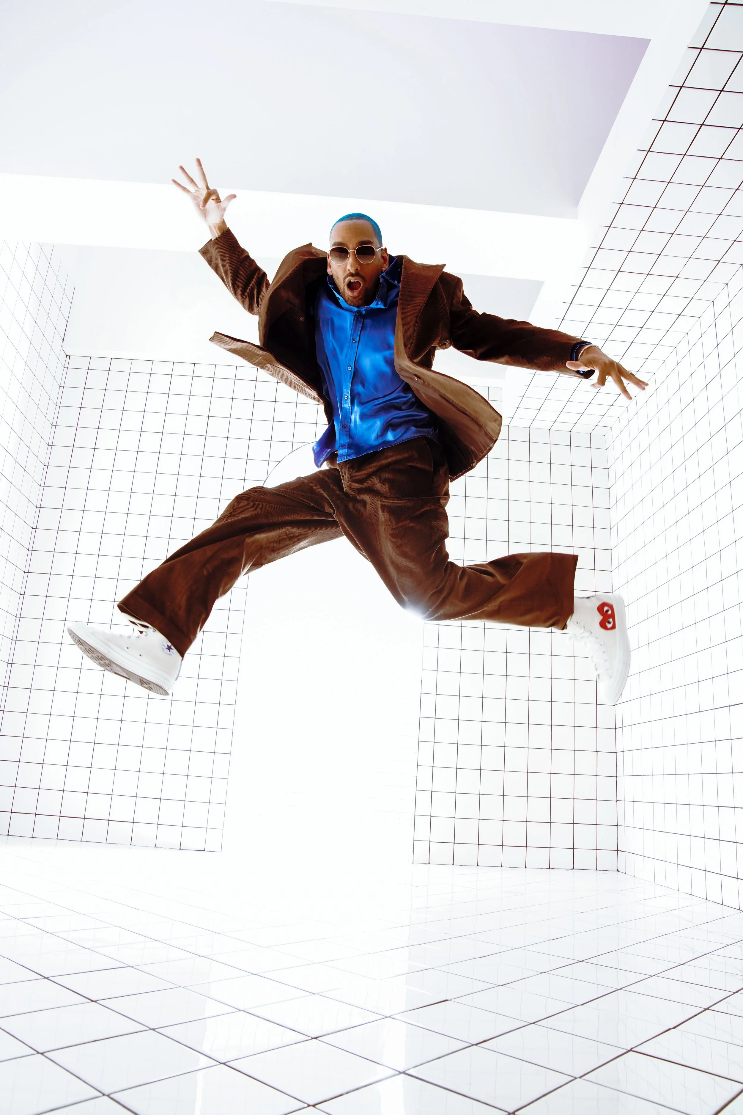 Man in brown suit jumping in a white, grid-lined room with a surprised expression.