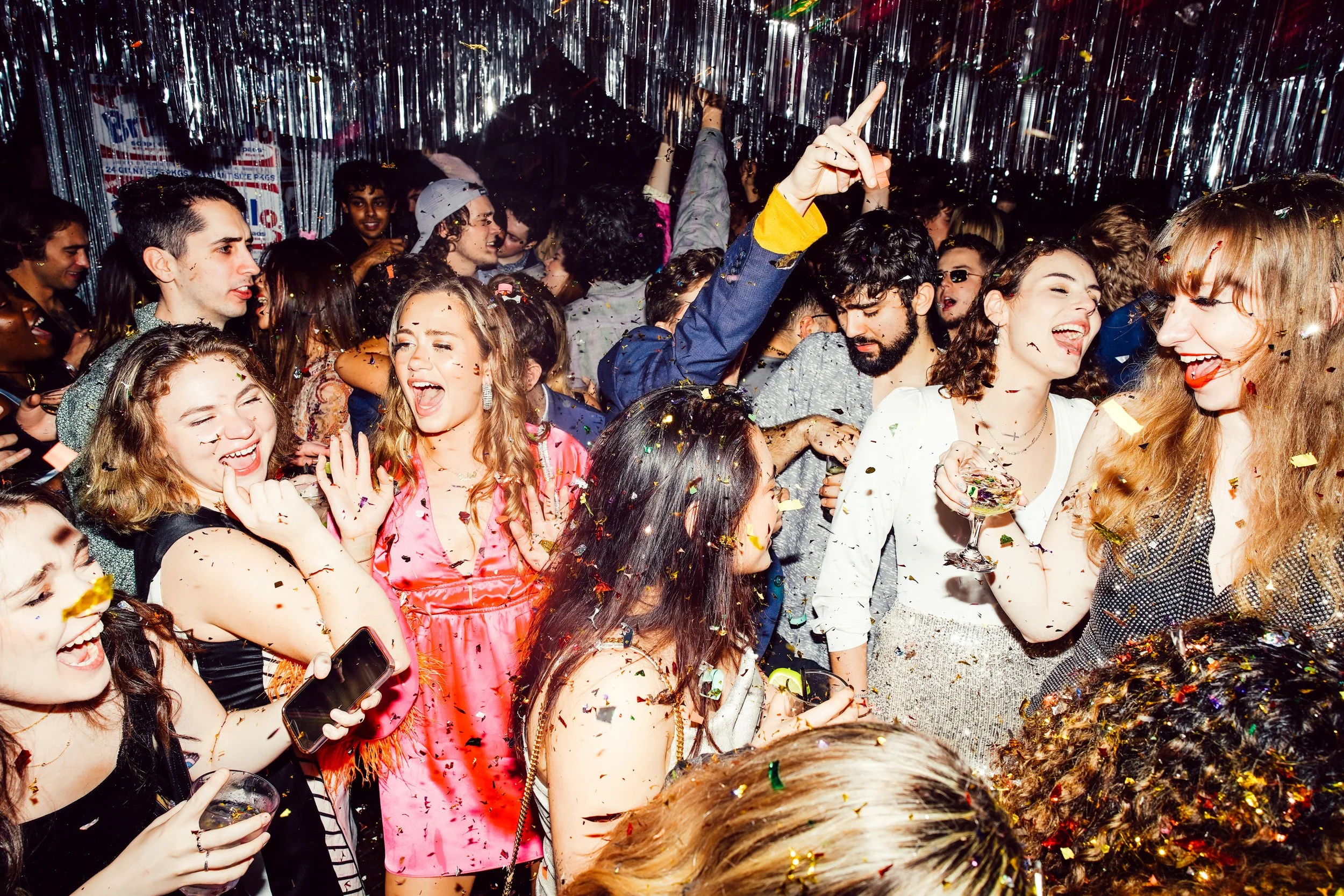 A lively party scene with young adults dancing, laughing, and enjoying a celebration with confetti and festive decorations.