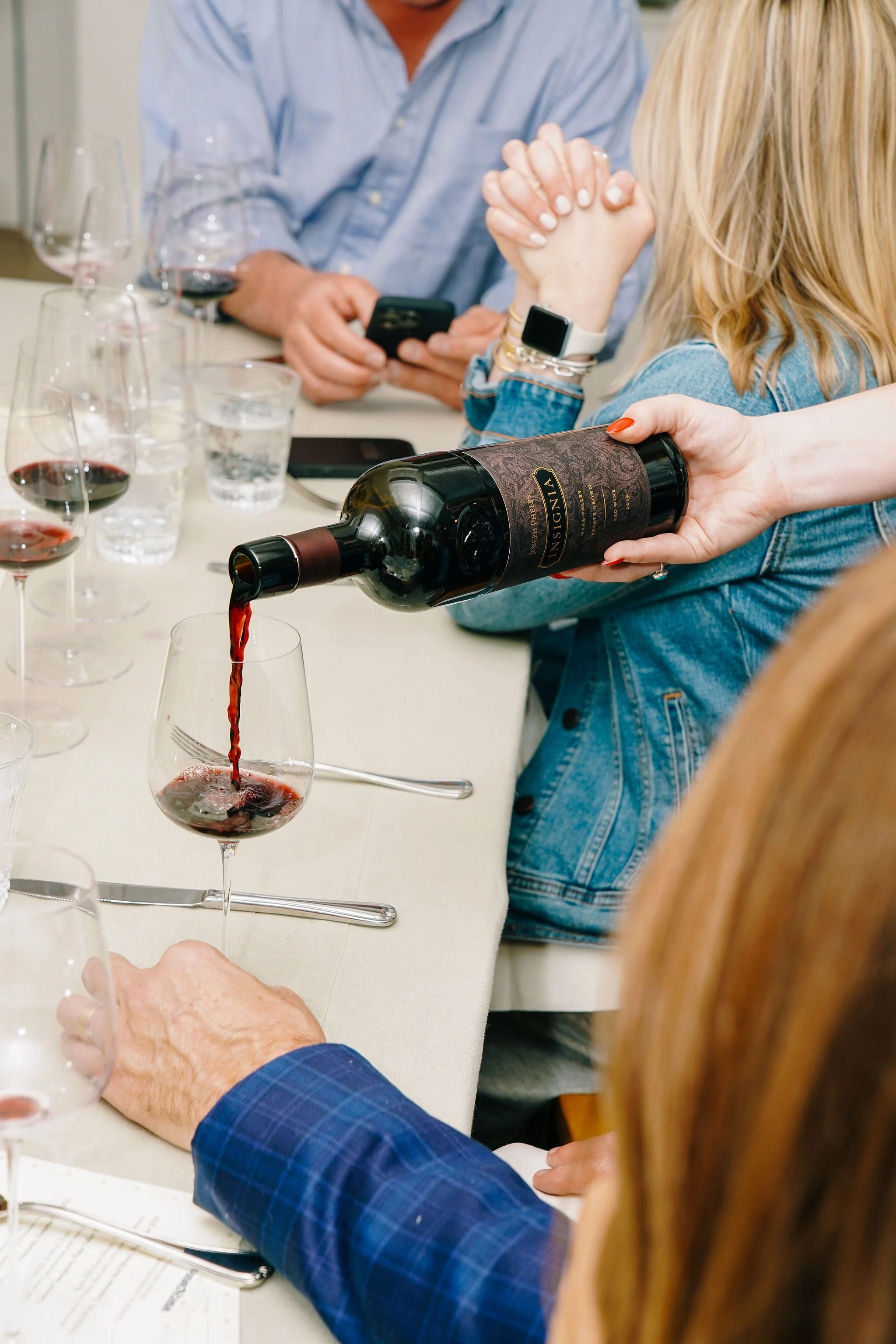 A woman is pouring red wine into a glass during a group dining experience.
