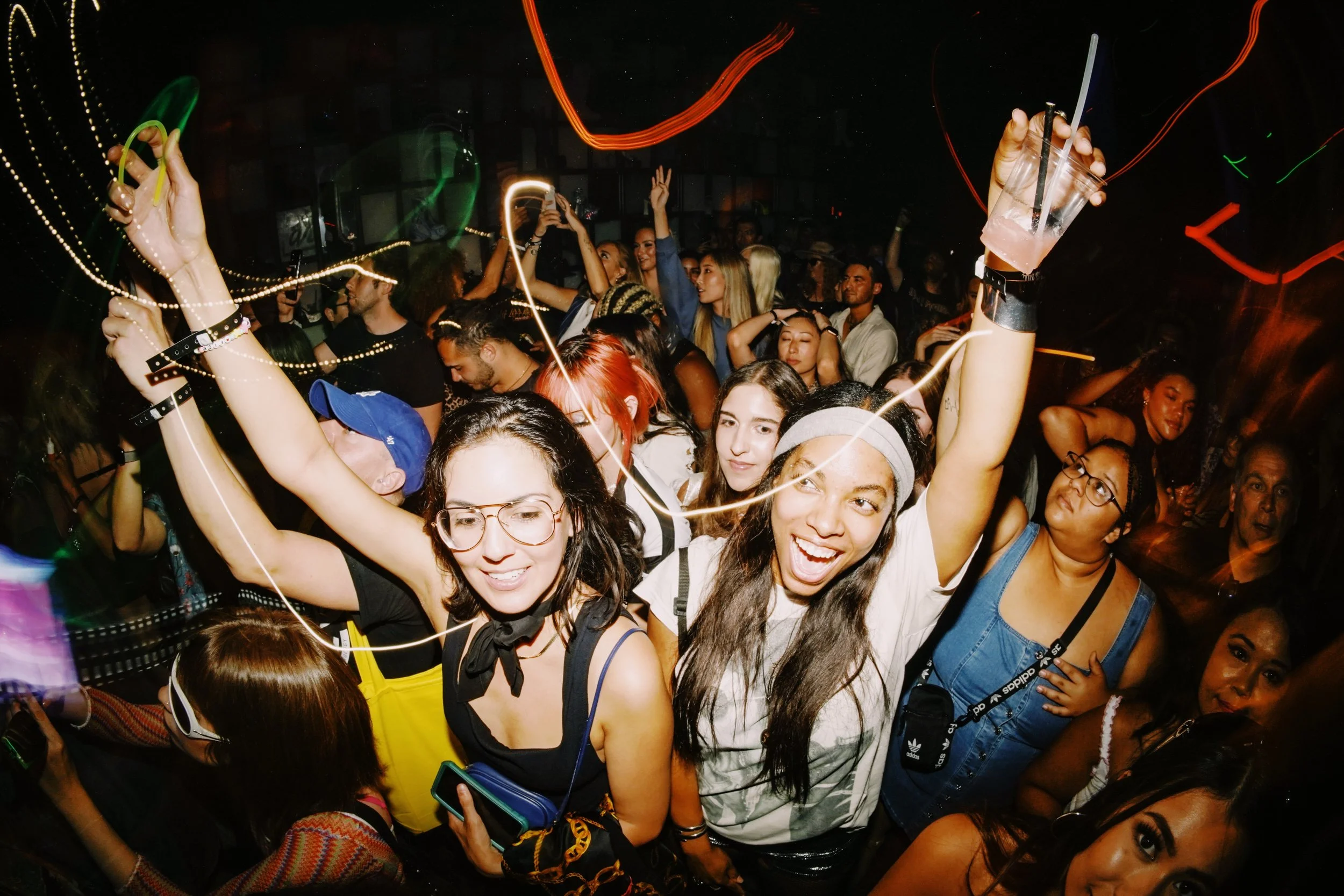 A group of people dancing and enjoying music at a nightclub with colorful lights and glow sticks.