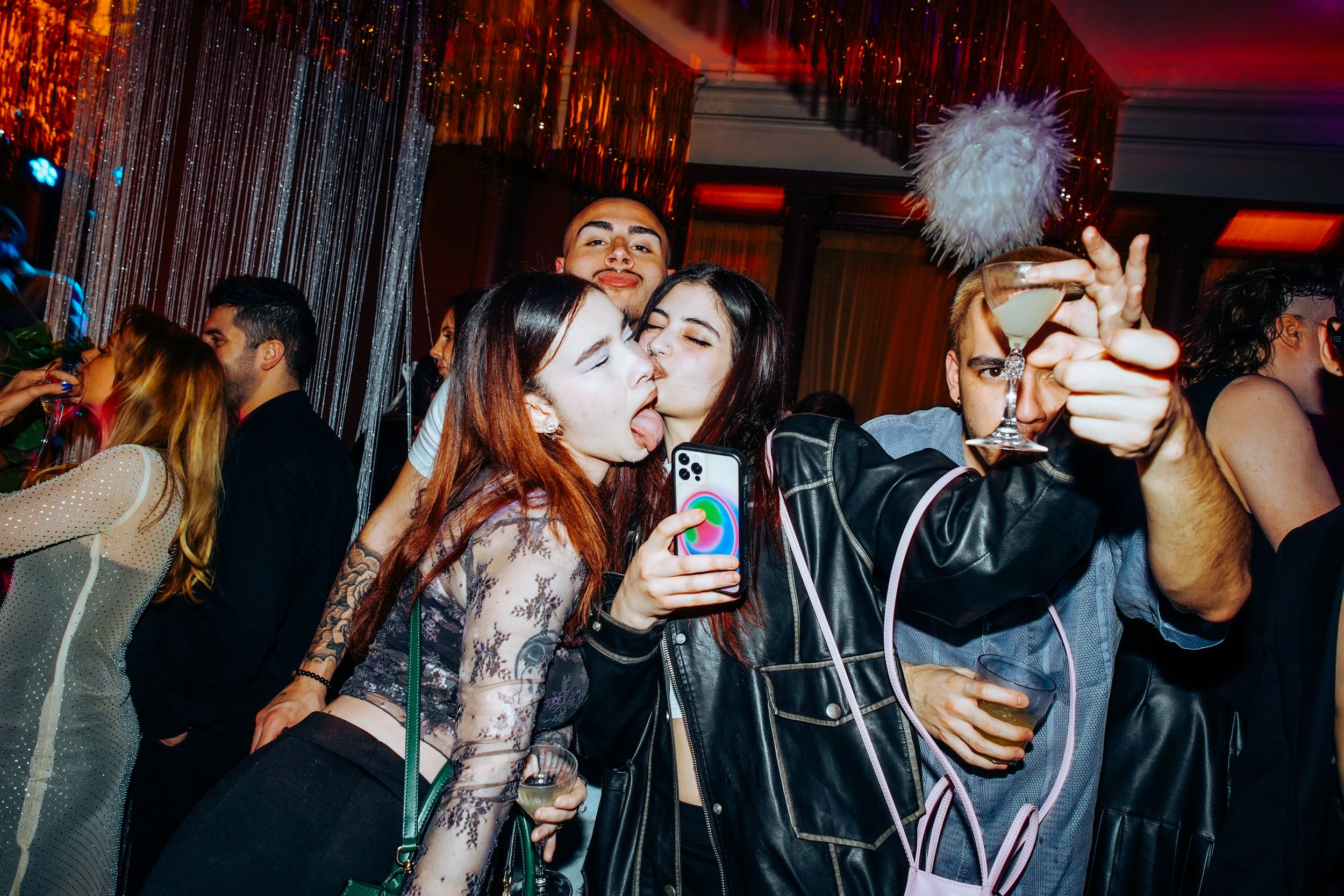 Group of young people partying and taking selfie at a nightclub with colorful lighting and decorations.