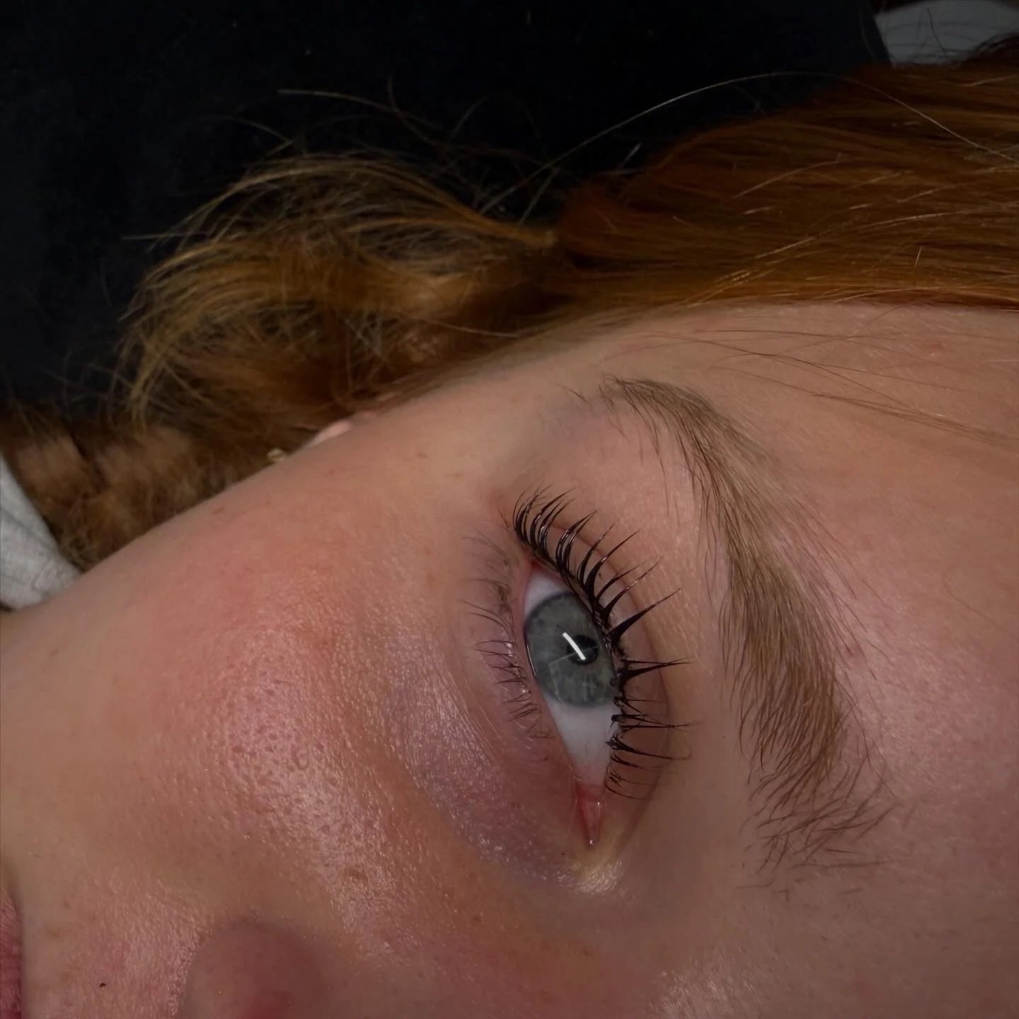 Close-up of a person's face focusing on the eye with long eyelashes, light eyebrows, and light red hair visible.