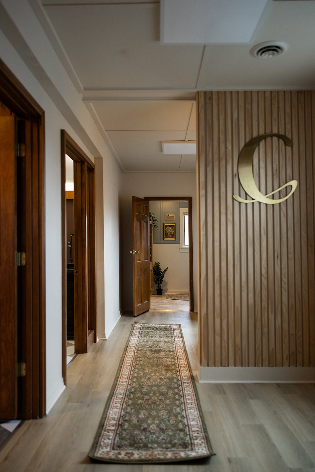 Interior hallway with wooden doors, a decorative rug, and a wooden accent wall with a metal crescent moon decor.