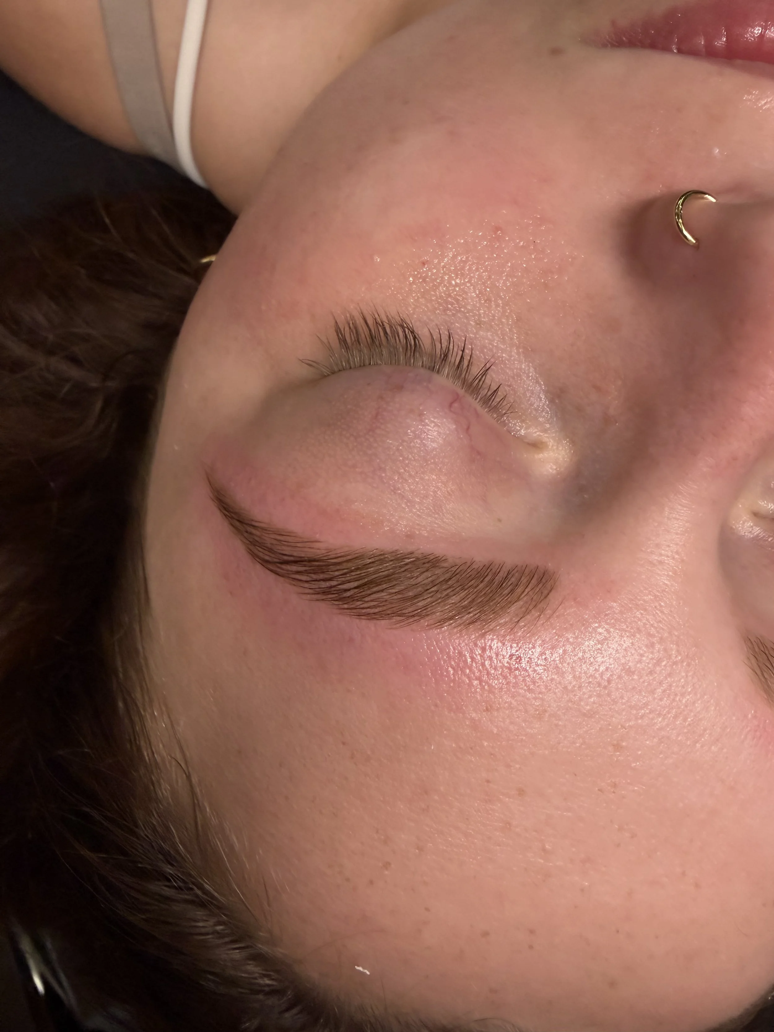Close-up of a person's face with closed eyes, gold nose ring, and natural skin texture.