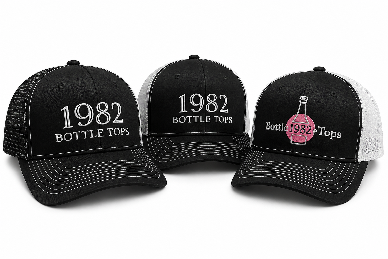 Three black and white trucker hats with embroidered designs celebrating 1982 and bottle tops, one with pink and gray embroidery and a bottle graphic.