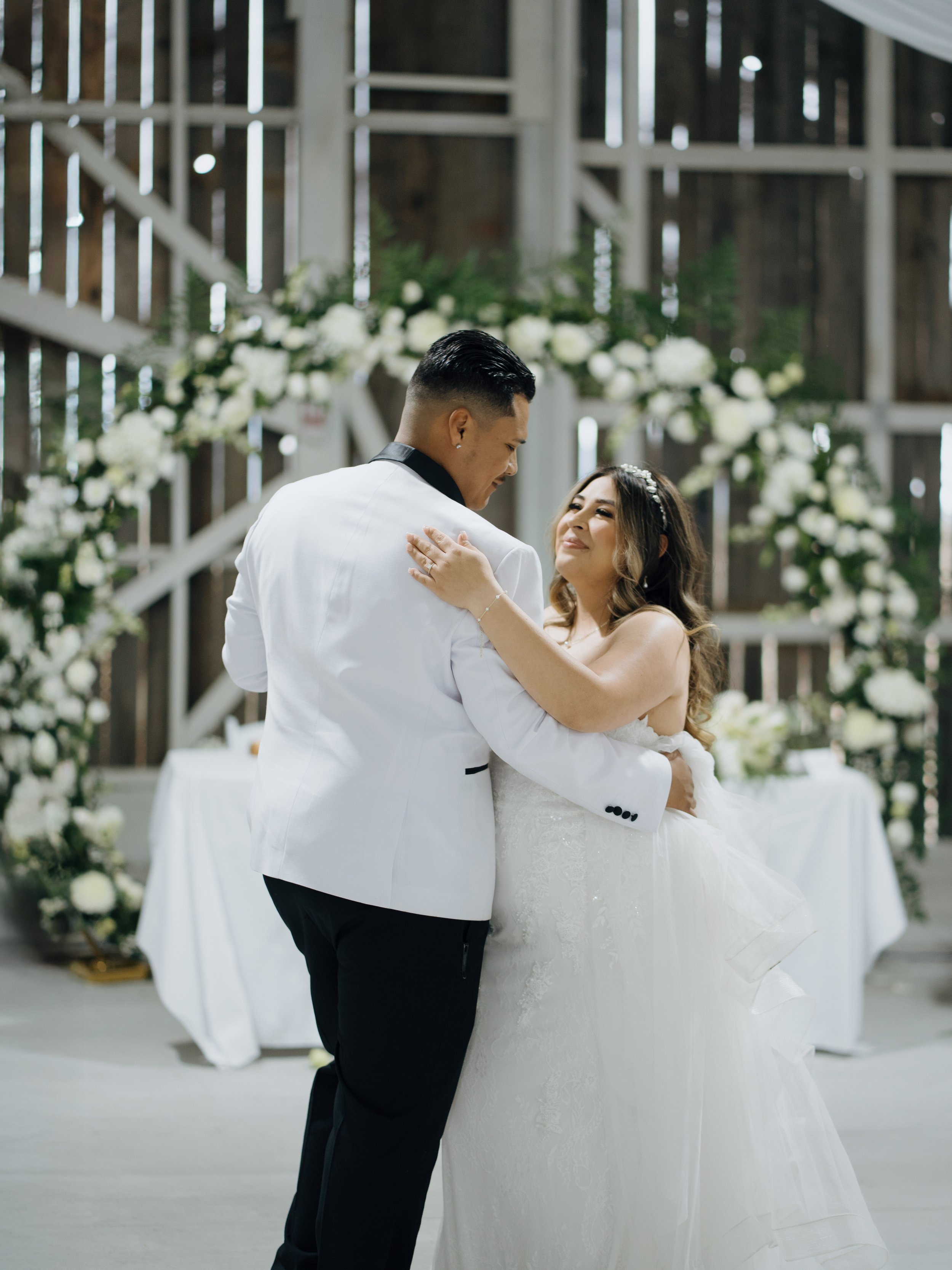 A bride and groom share a dance at their wedding ceremony in a rustic venue with wood walls and floral decorations.