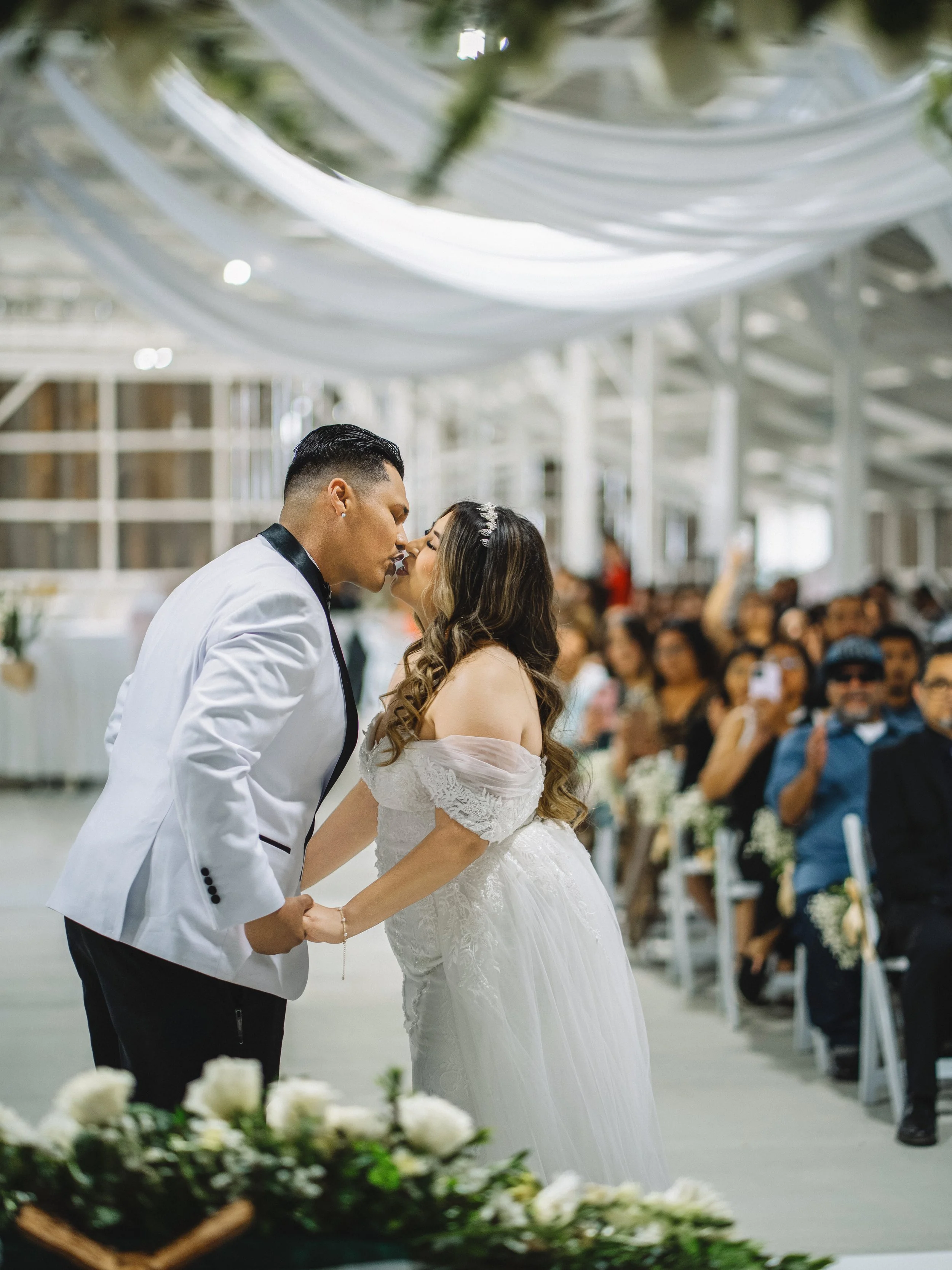A bride and groom kissing during their wedding ceremony inside a decorated venue.