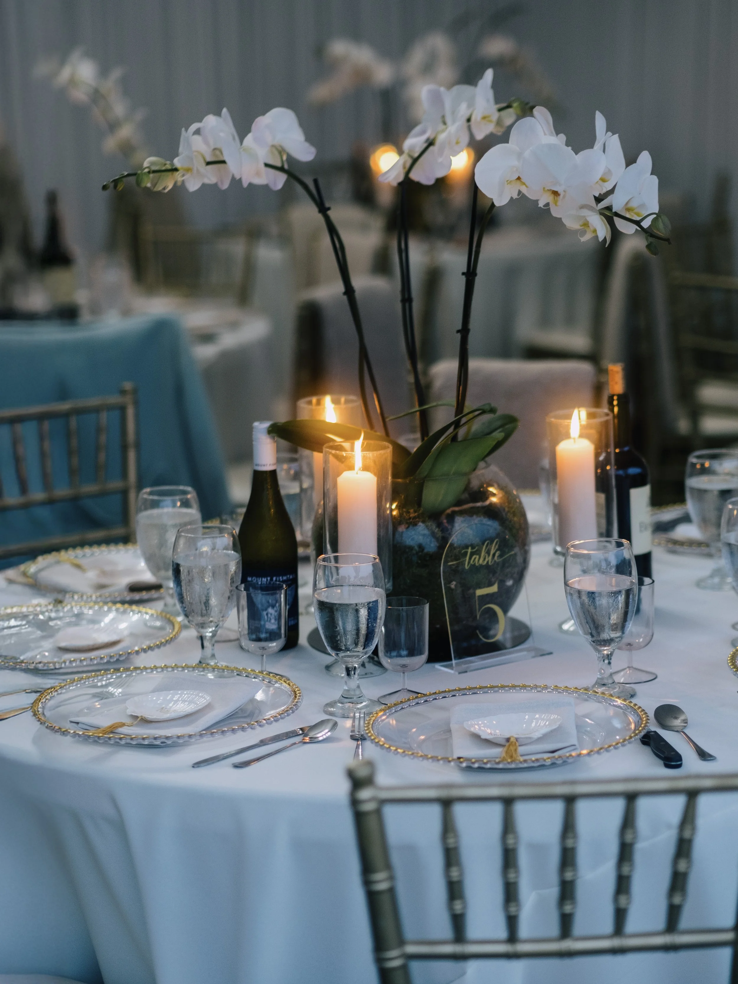 Elegant table setting with white plates, wine glasses, candles, and an orchid centerpiece at a formal event.