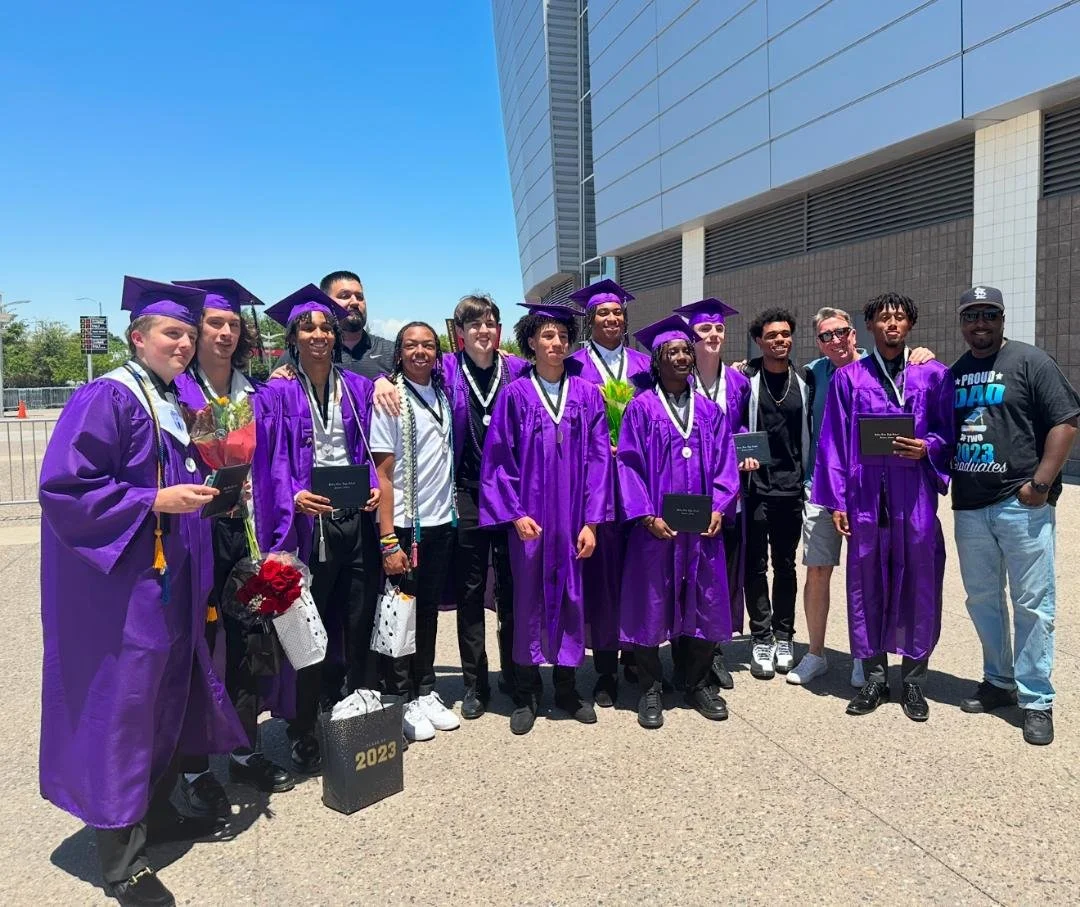 Dr. Neal posing with a group of graduates in purple caps and gowns