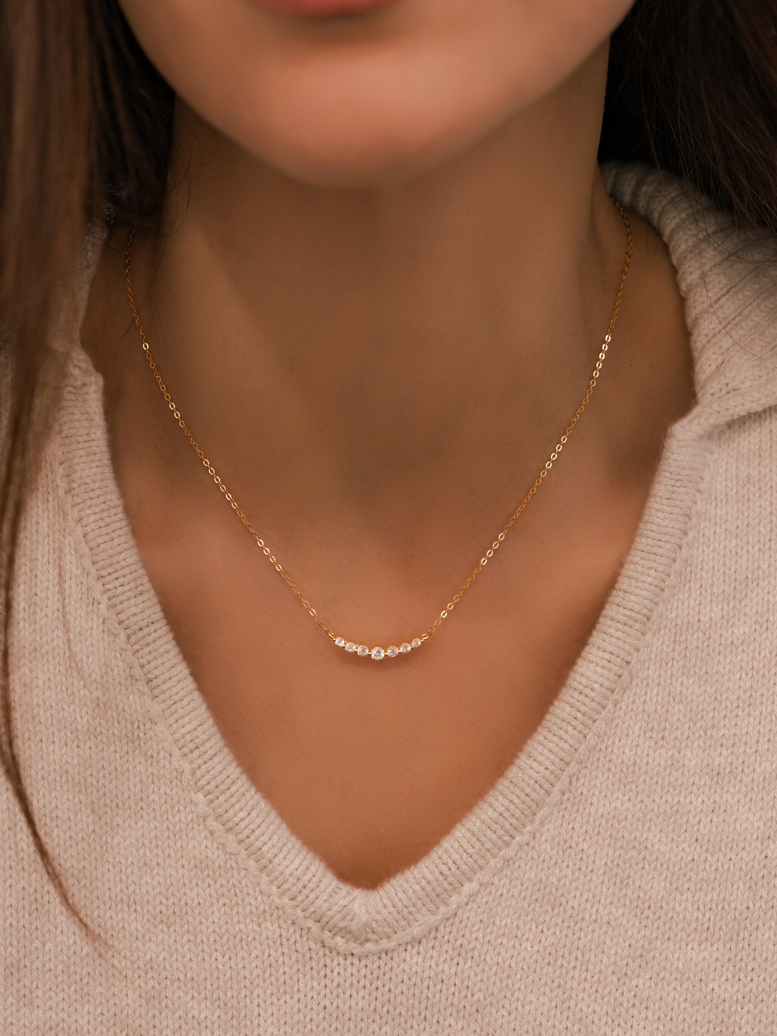 On-model jewelry photography showcasing a delicate gold diamond arc necklace in a clean, elevated setting over a cream knit sweater.