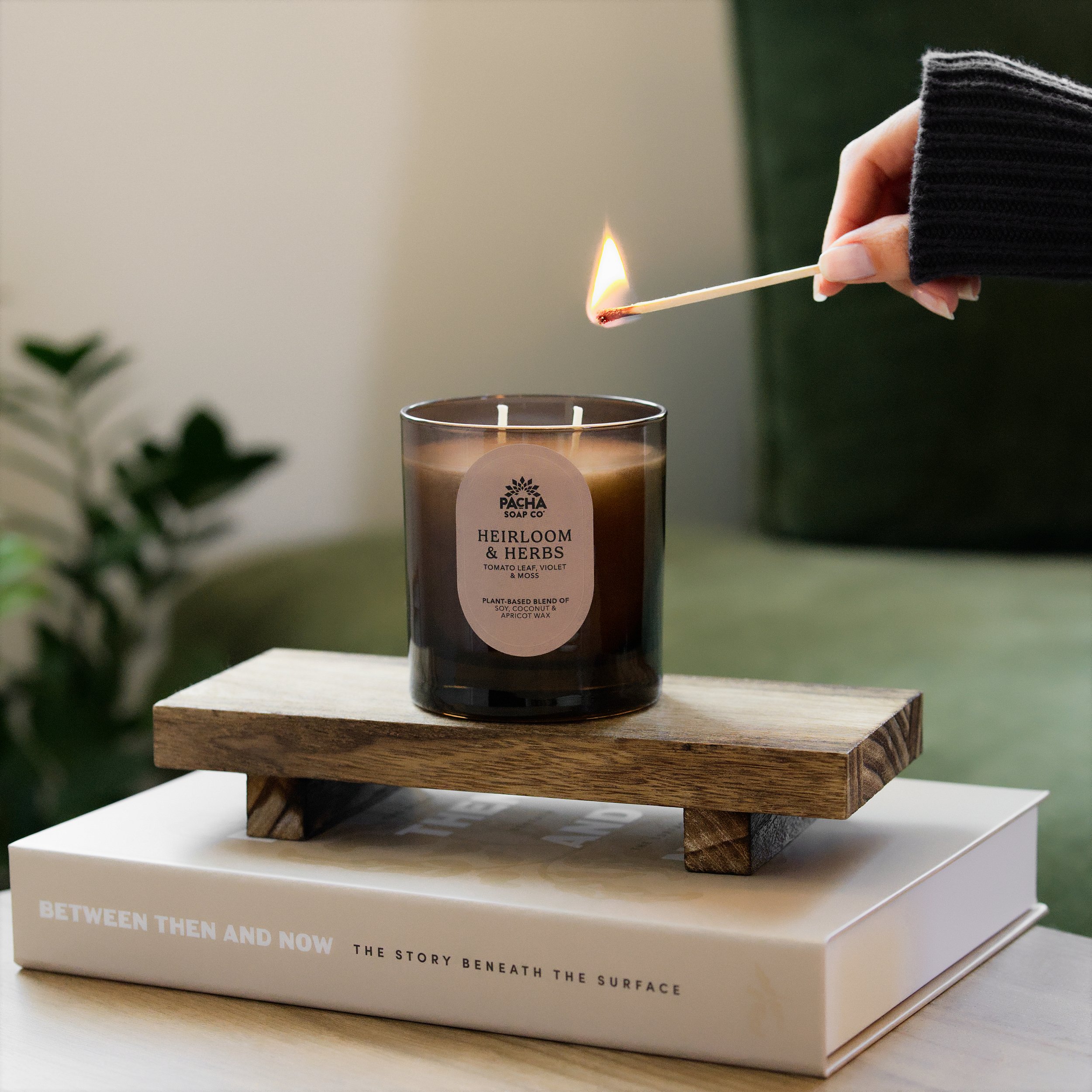 Indoor luxury lifestyle photography of a Lit Maplewood & Bergamot scented candle in a dark glass jar on a marble surface, with dried orange slices and a wooden bowl in the background.