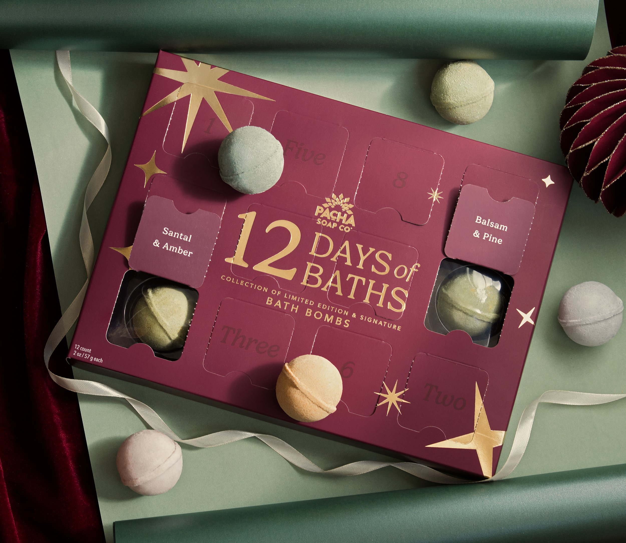 Elevated backdrop photography shot of 12 Days of Baths holiday advent calendar with assorted bath bombs on green wrapping paper with ribbon.