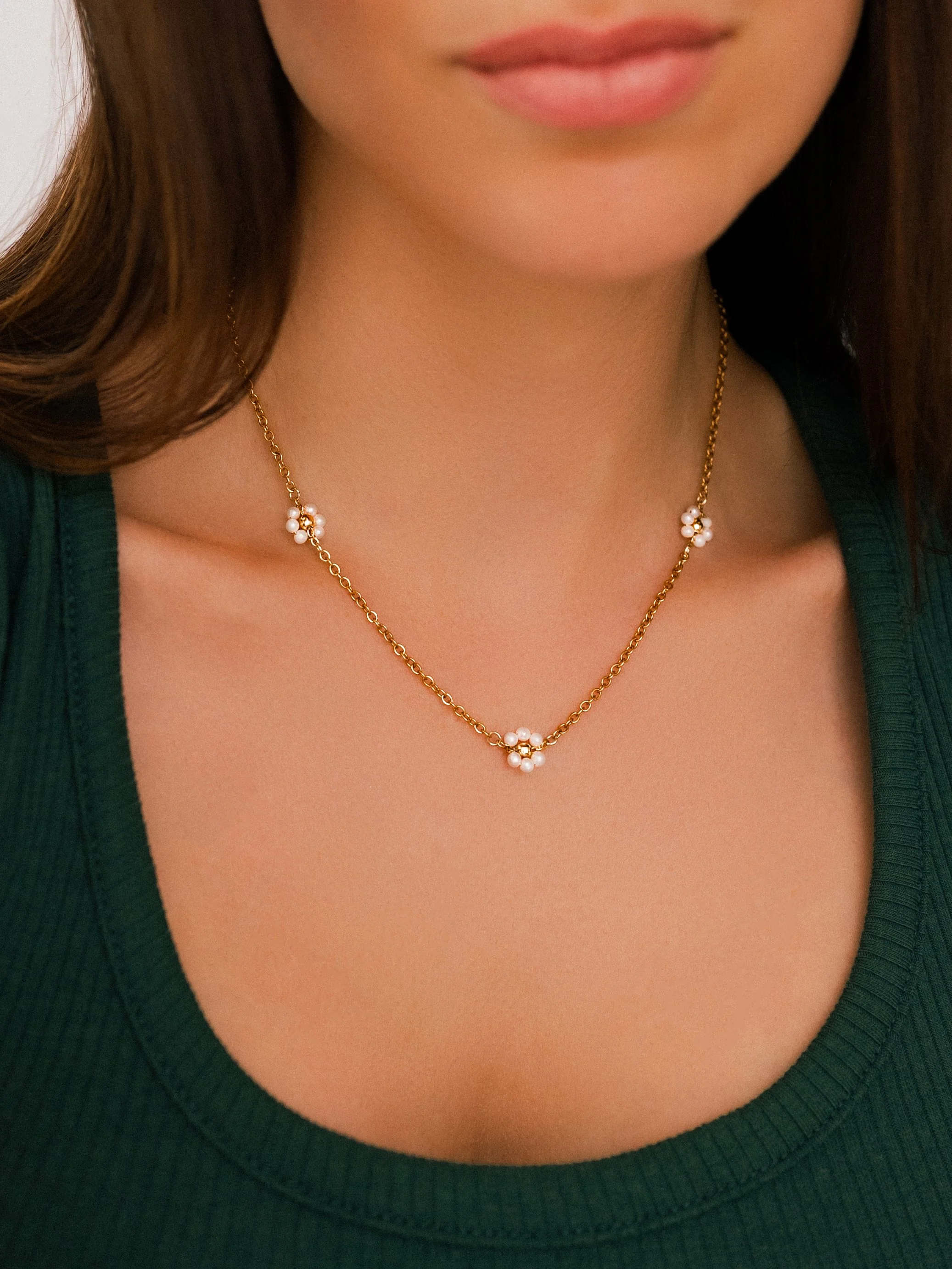 Elevated on-model product photography close-up of a model wearing a delicate gold chain necklace with white pearl floral accents.