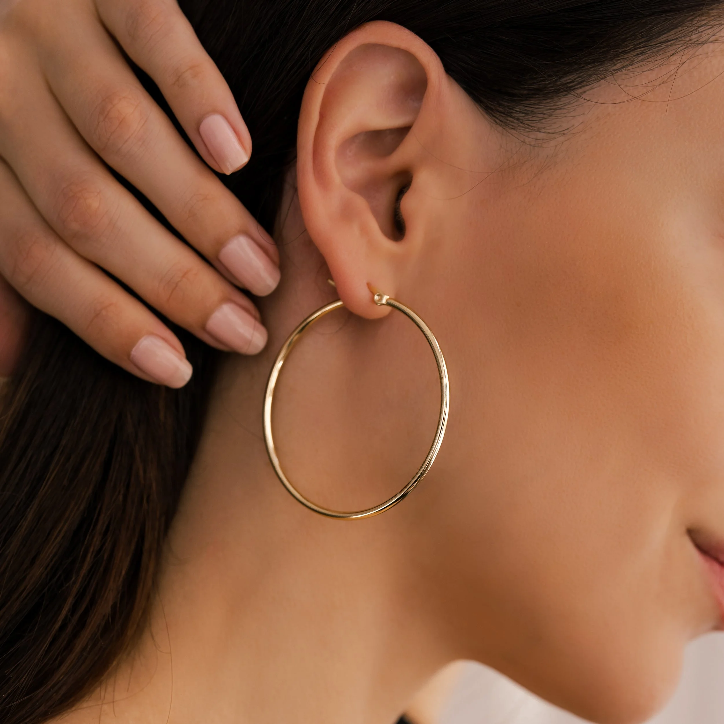 On-model jewelry photography showcasing bold gold hoop earrings worn by a model in a clean, elevated studio setting.