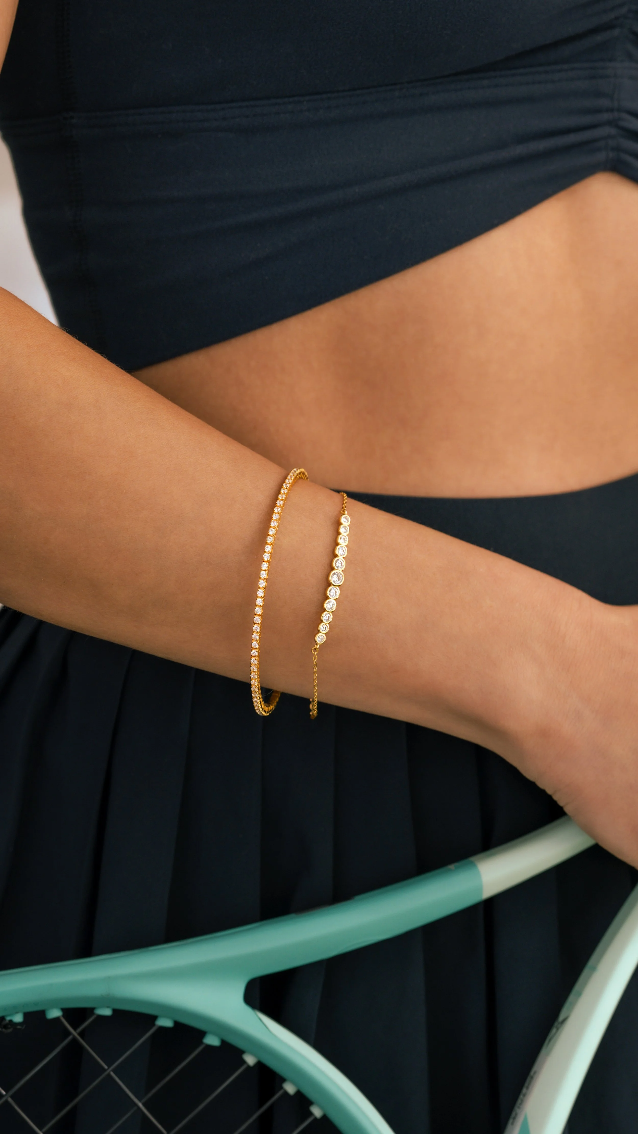 Elevated on-model jewelry photography showcasing dainty gold tennis bracelets on a woman wearing a tennis outfit in a clean studio setting.
