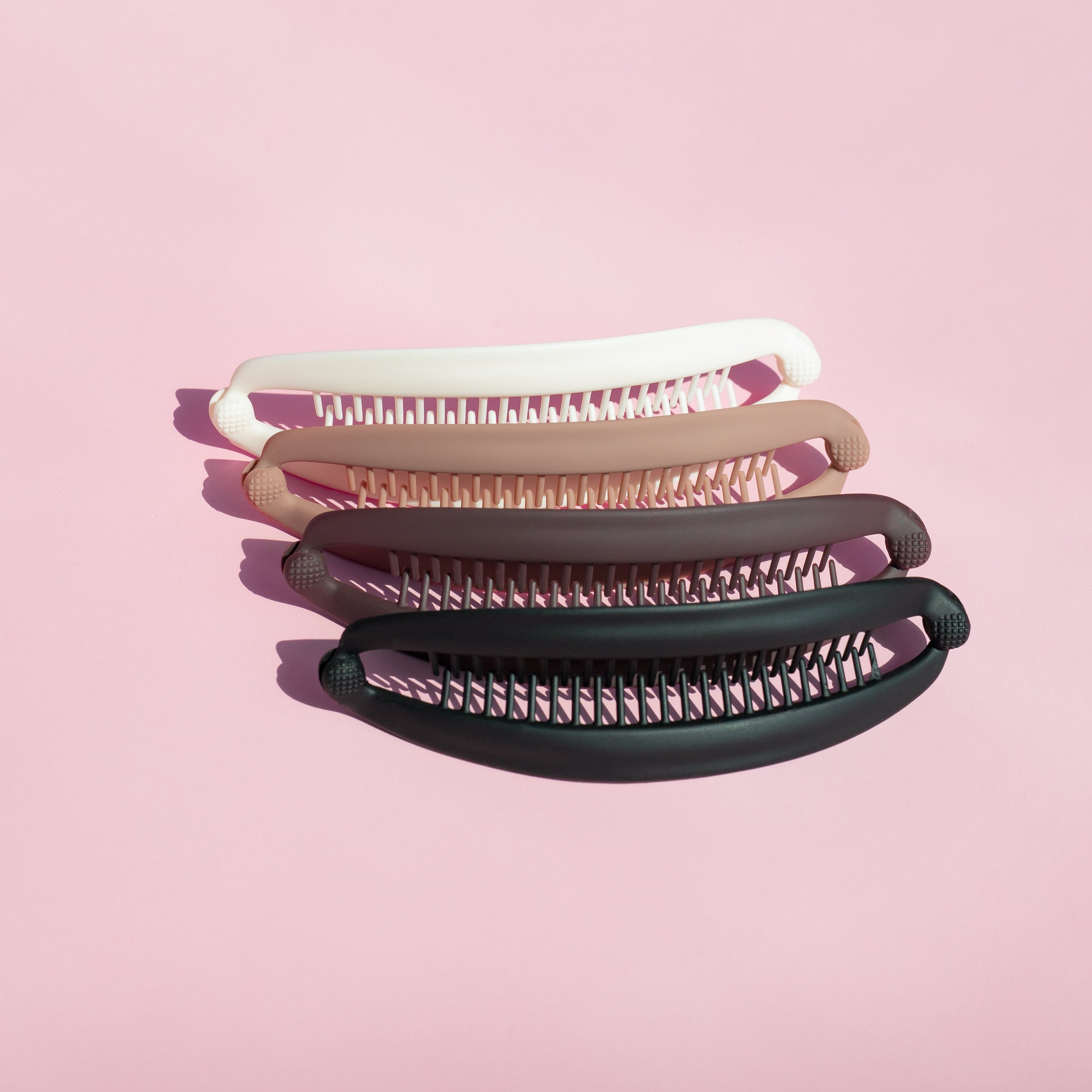 Four hairbrushes in white, beige, dark gray, and black arranged on a pink background.