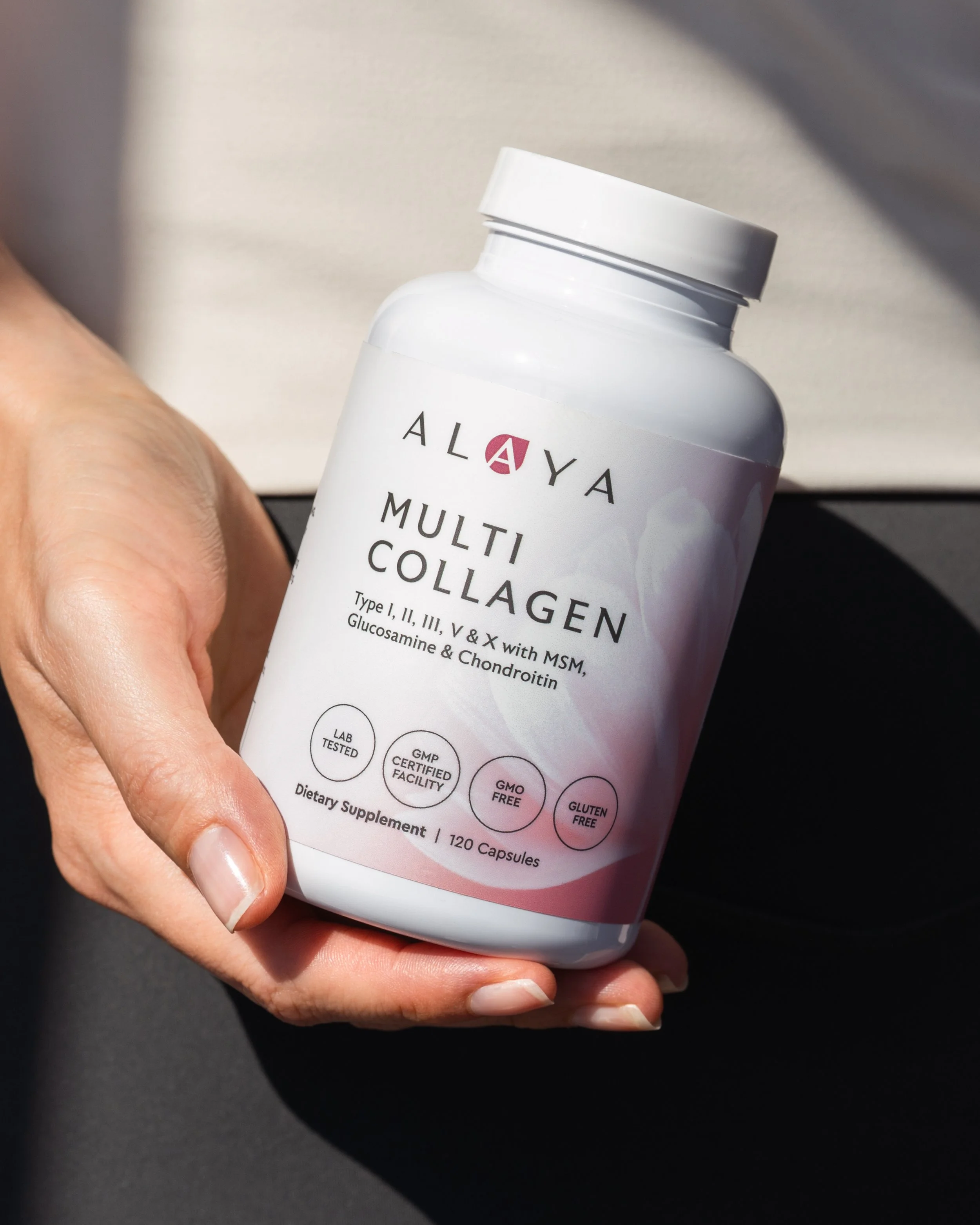Elevated product photography of a hand model holding a bottle of a multi-collagen dietary supplement capsules with glucosamine, chondroitin, and MSM with shadows behind.
