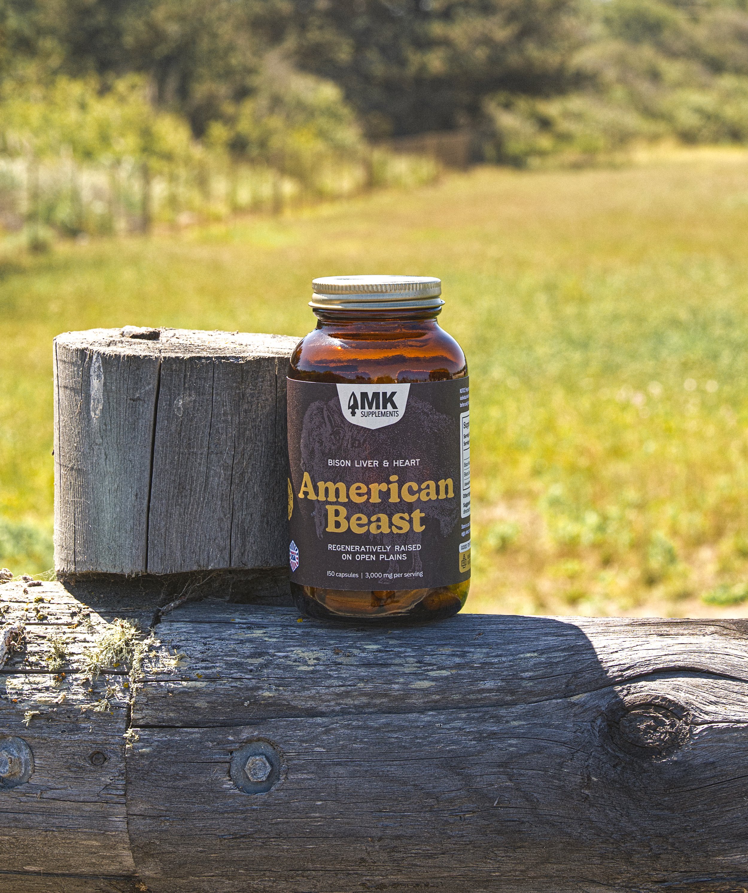 Outdoor lifestyle product photography for a supplement brand with bison liver and heart supplement bottle on a weathered wooden fence outdoors on a field.