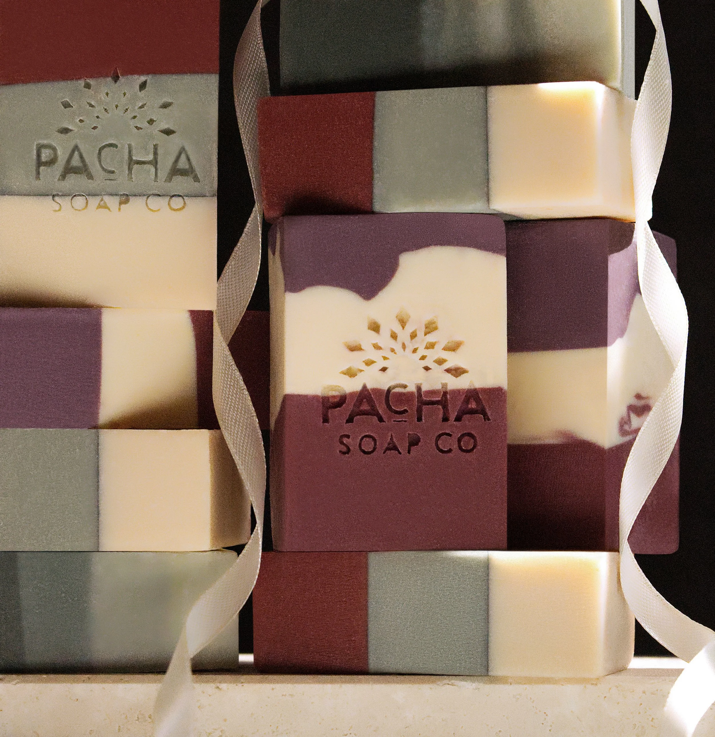Elevated product photography of colorful stacked handmade soap bars arranged with white ribbon on a dark backdrop.