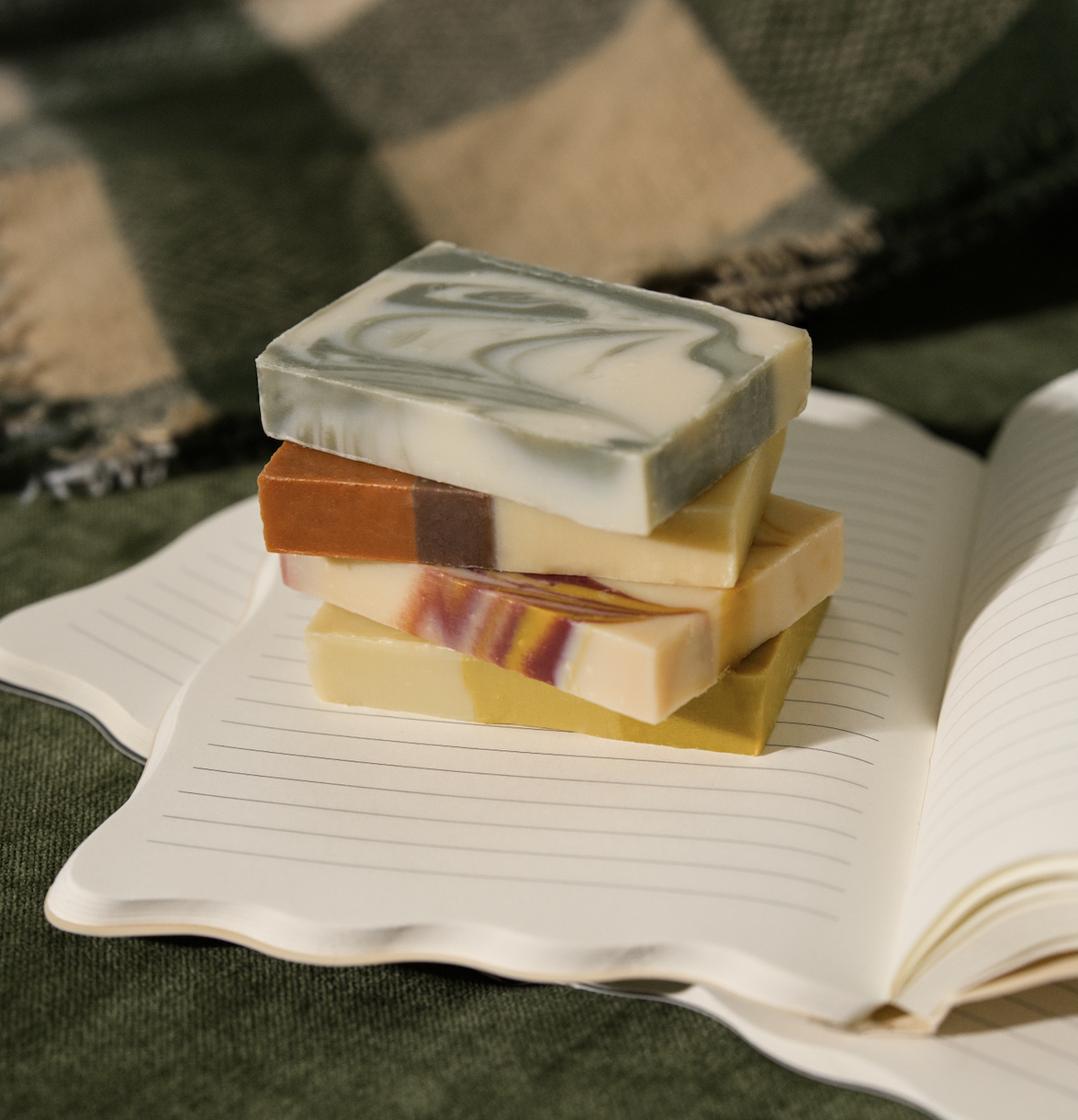 Beautiful stack of handmade artisan soap bars with colorful swirls on an open lined notebook in a luxury home setting.