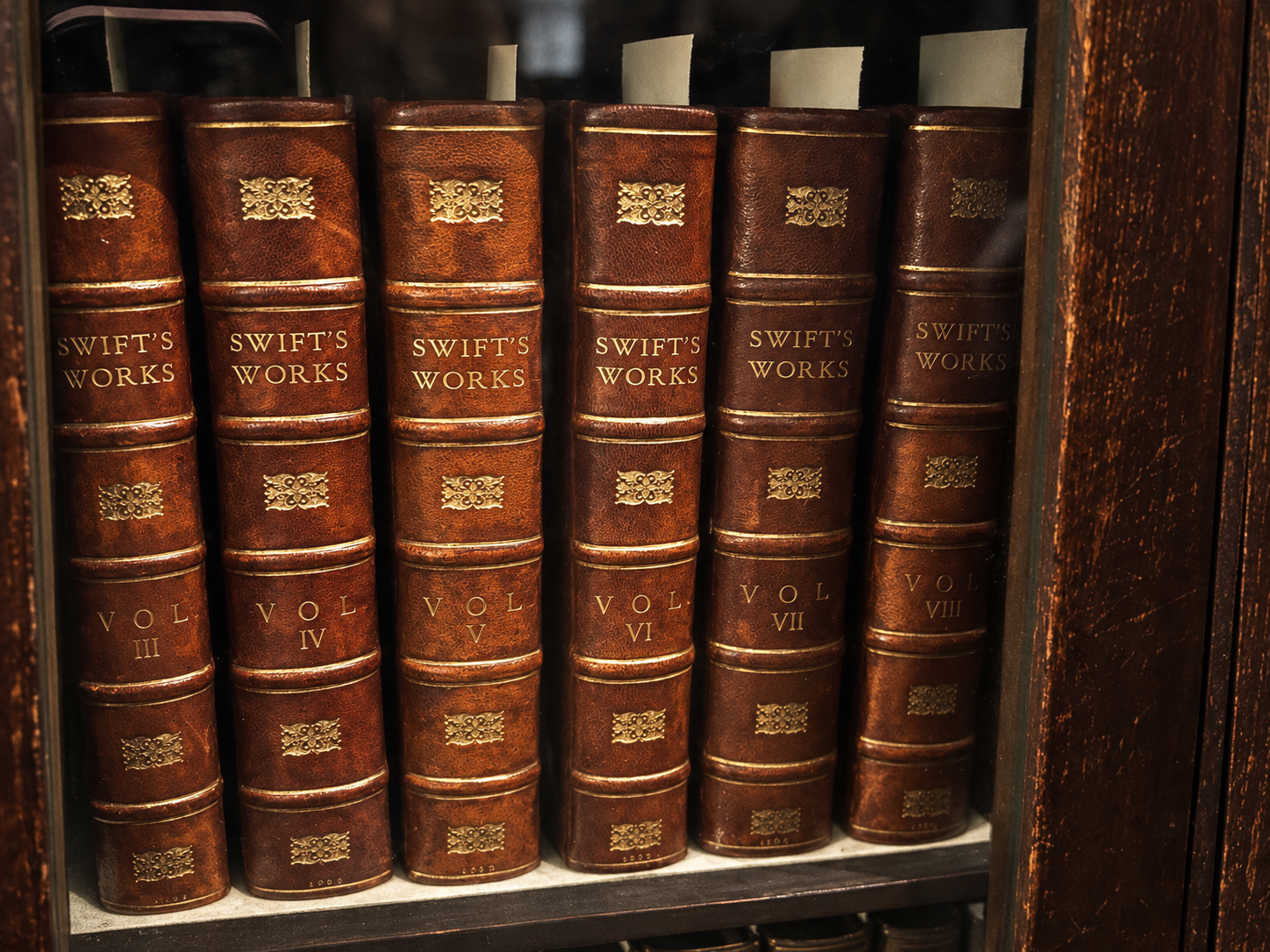 A row of vintage leather-bound books titled 'Swift's Works' on a shelf.
