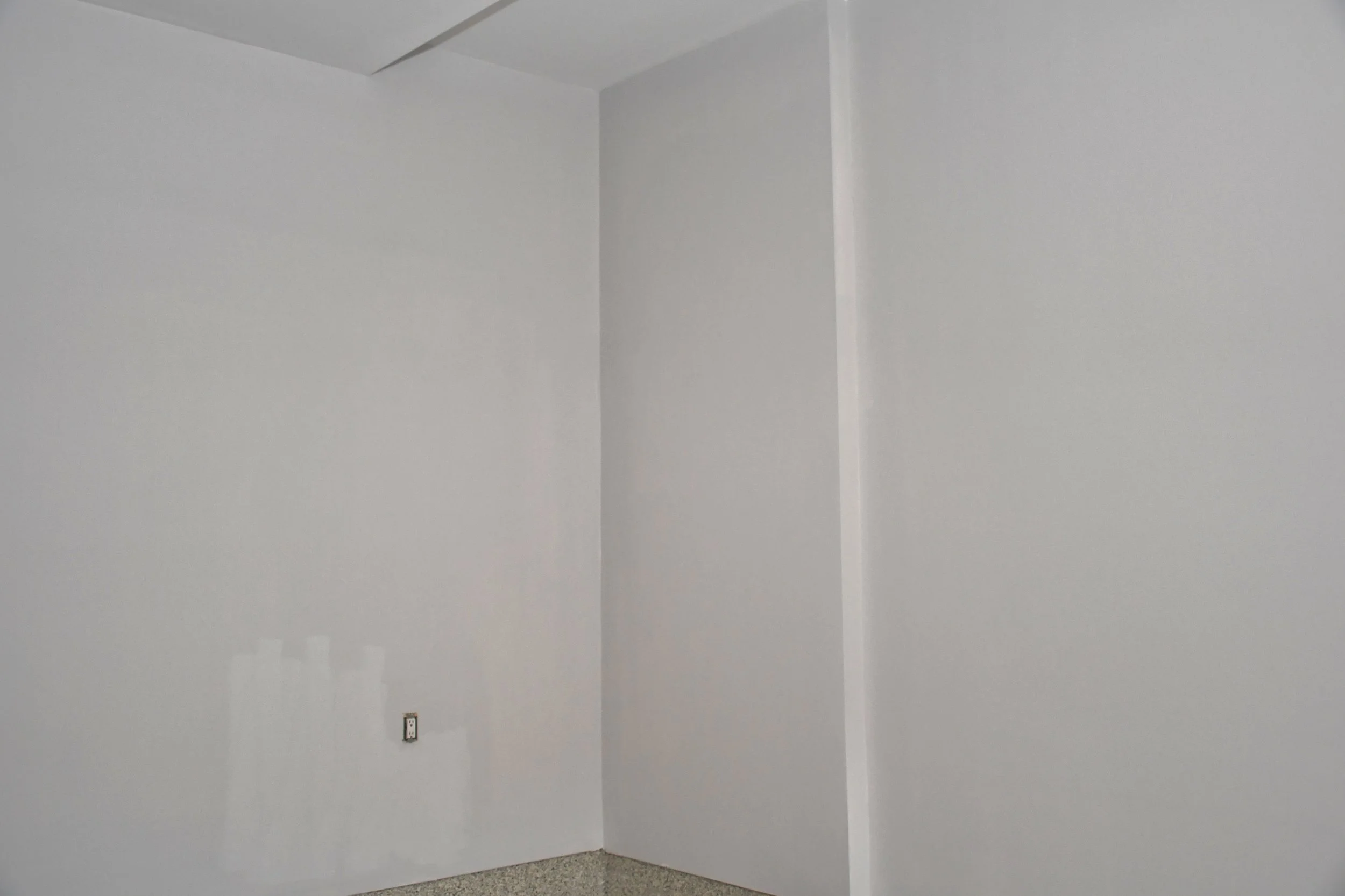 Empty room with white walls and a small electrical outlet near the floor.