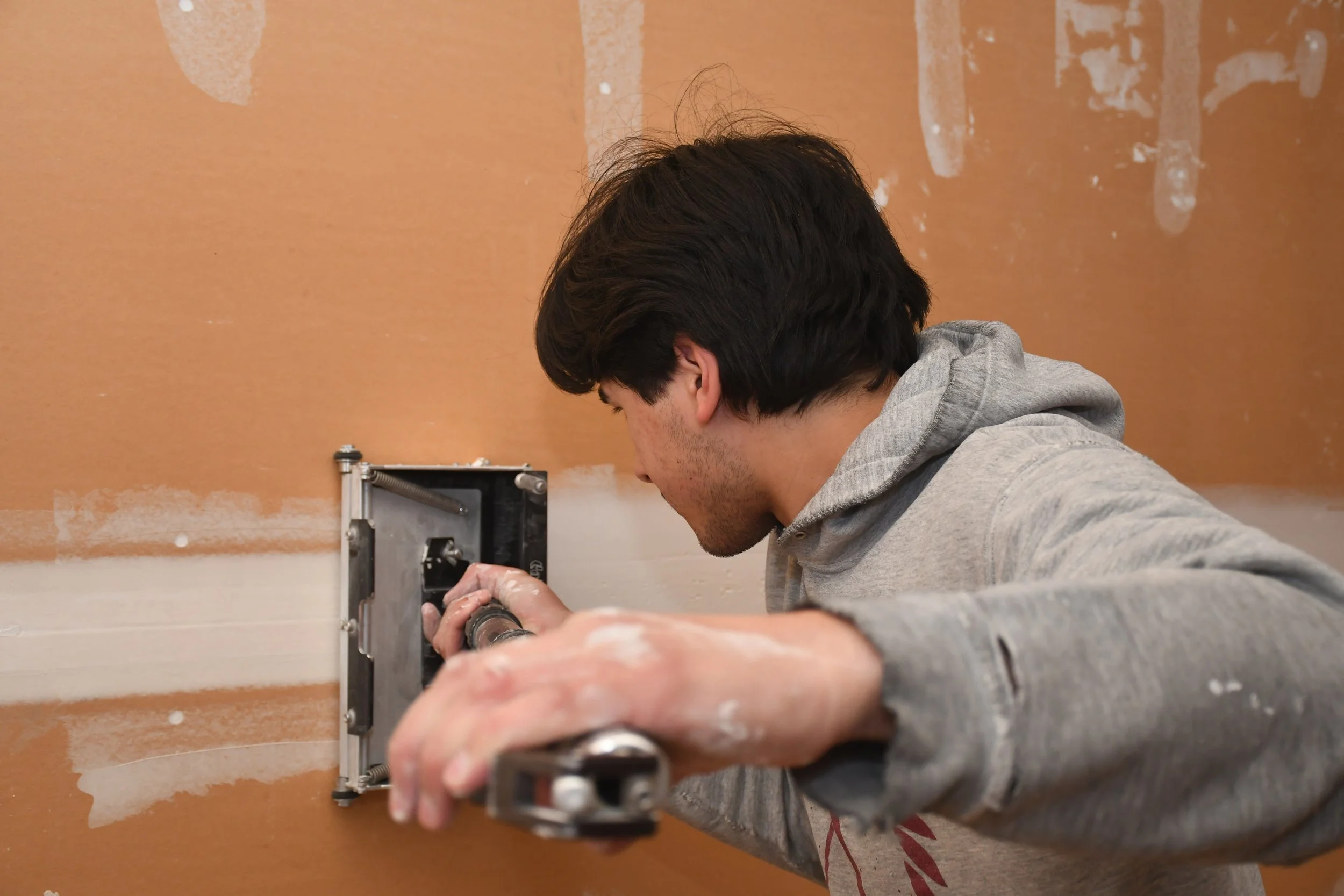 A person wearing a gray hoodie installing or repairing an electrical outlet in a wall.
