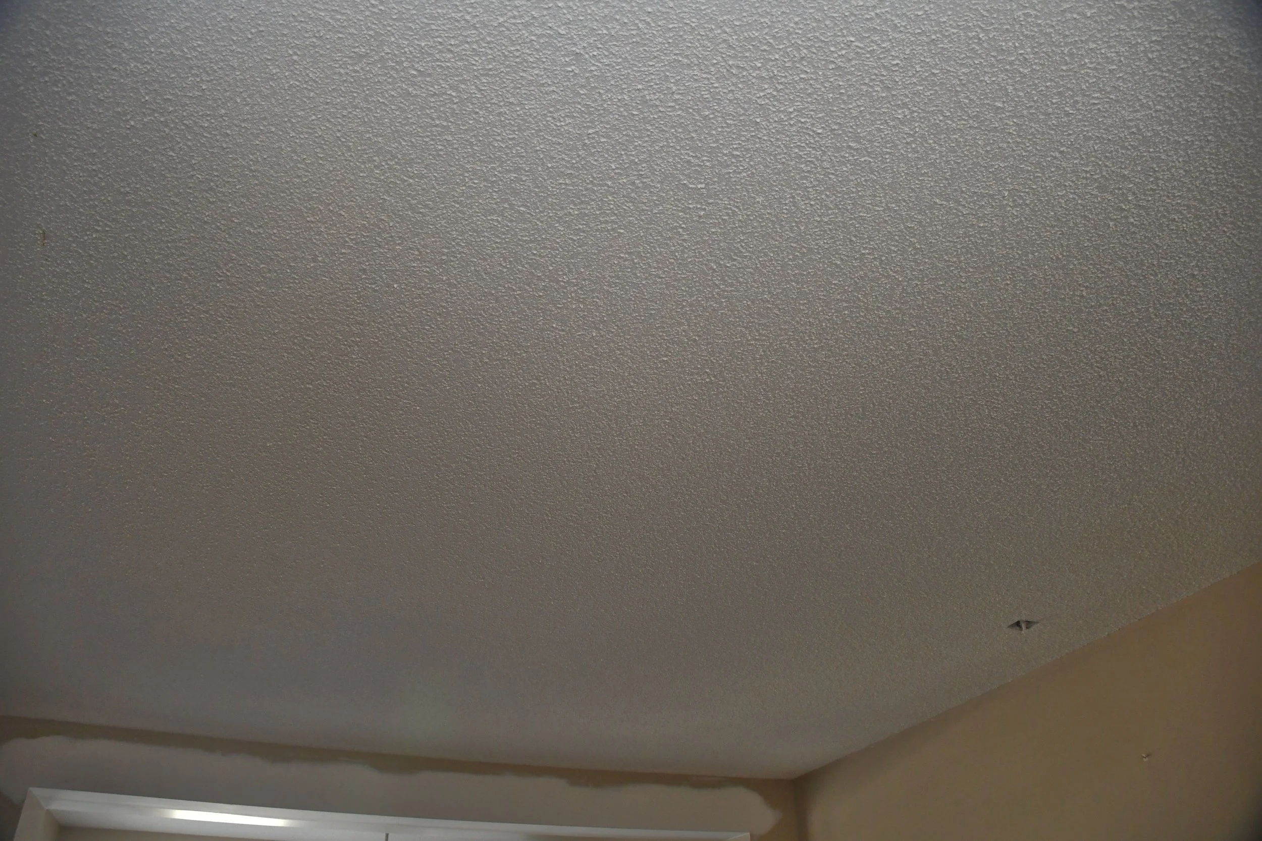 Ceiling with popcorn texture and a small hole, with part of a window frame visible at the bottom.