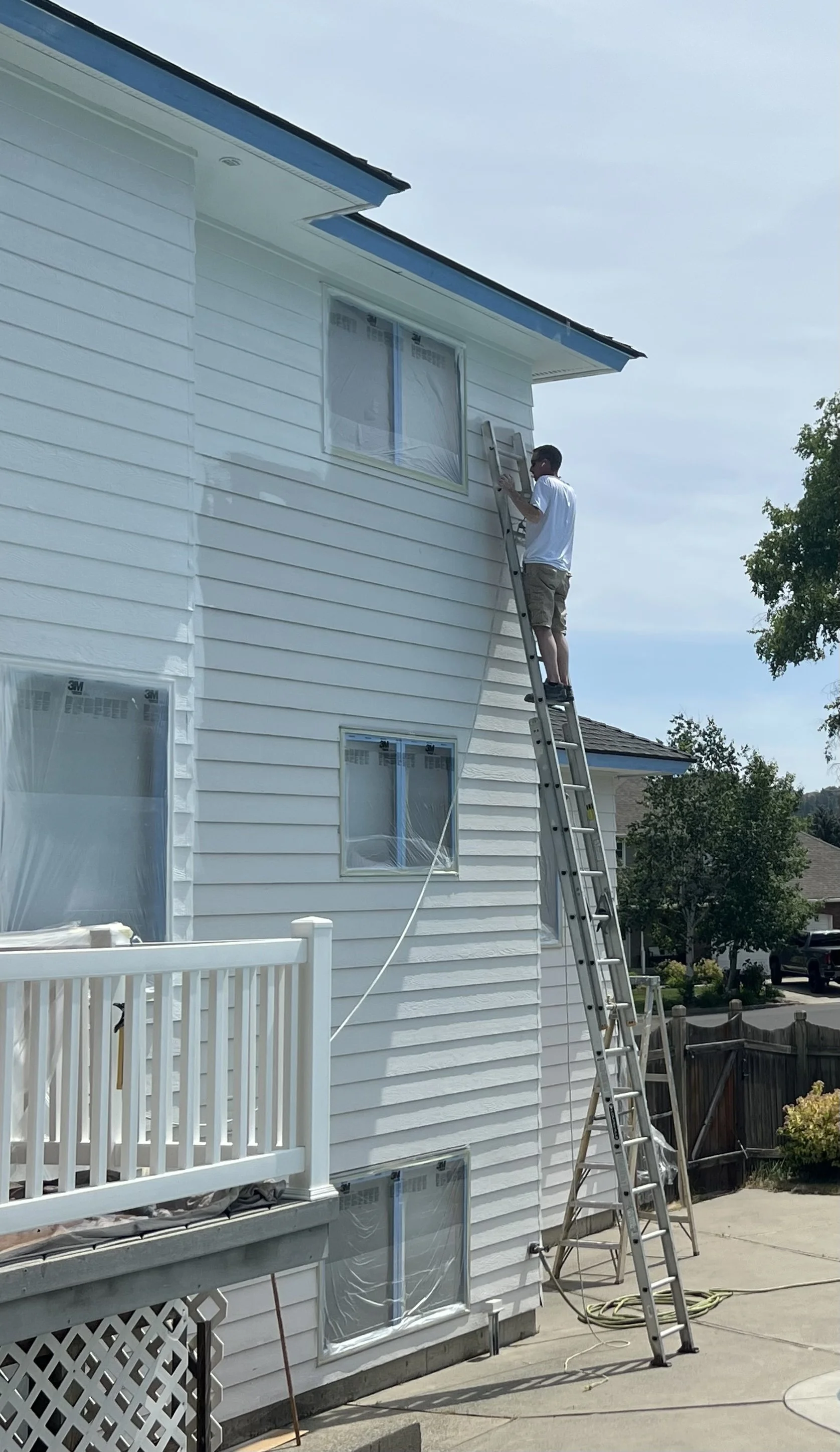 man standing on a ladder,  painting a white three story home
