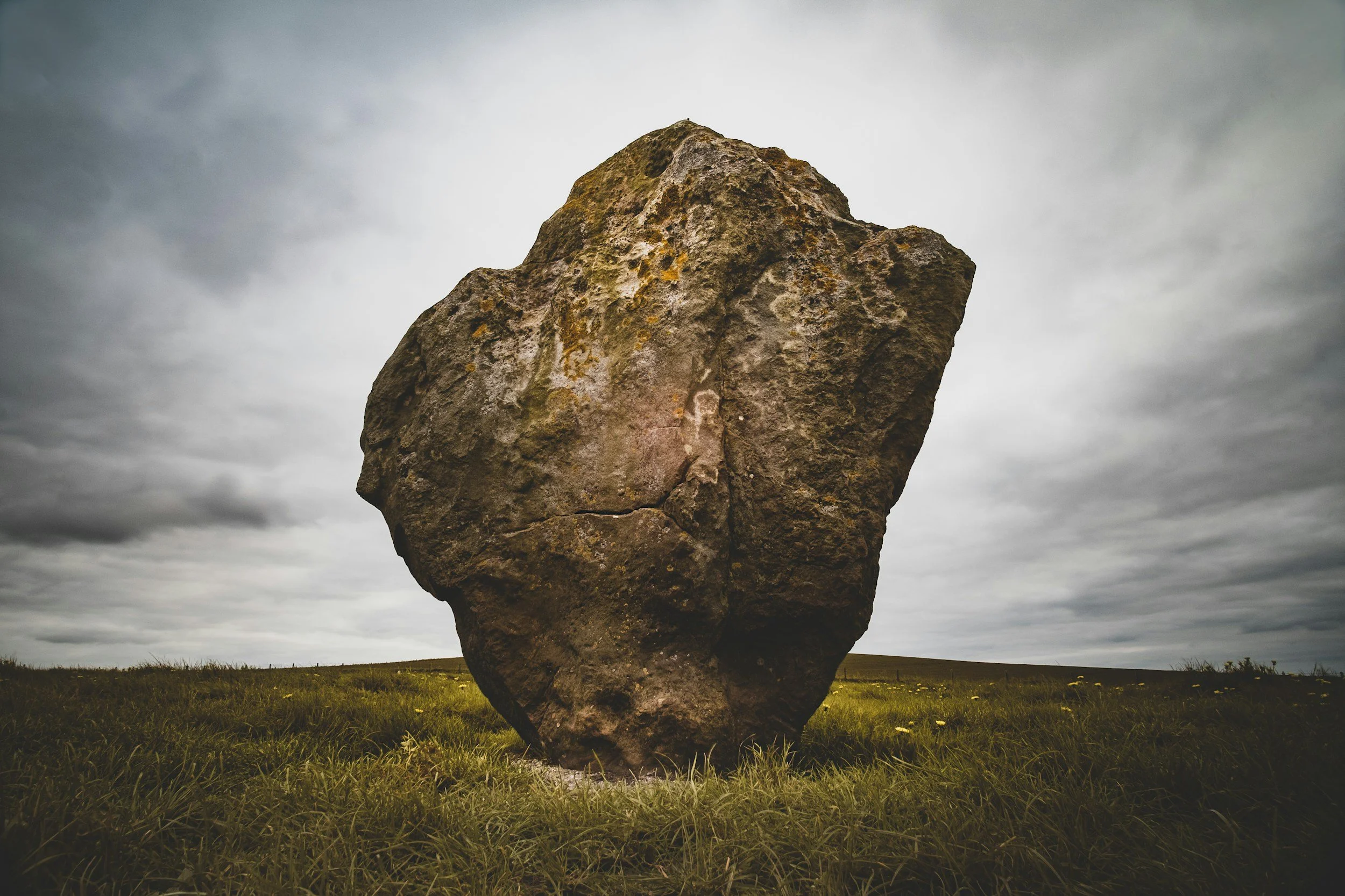 Large weathered boulder standing firmly in an open field under a cloudy sky—symbolizing emotional strength, resilience, and the sturdy therapeutic space therapists need to process and release the weight of their work.