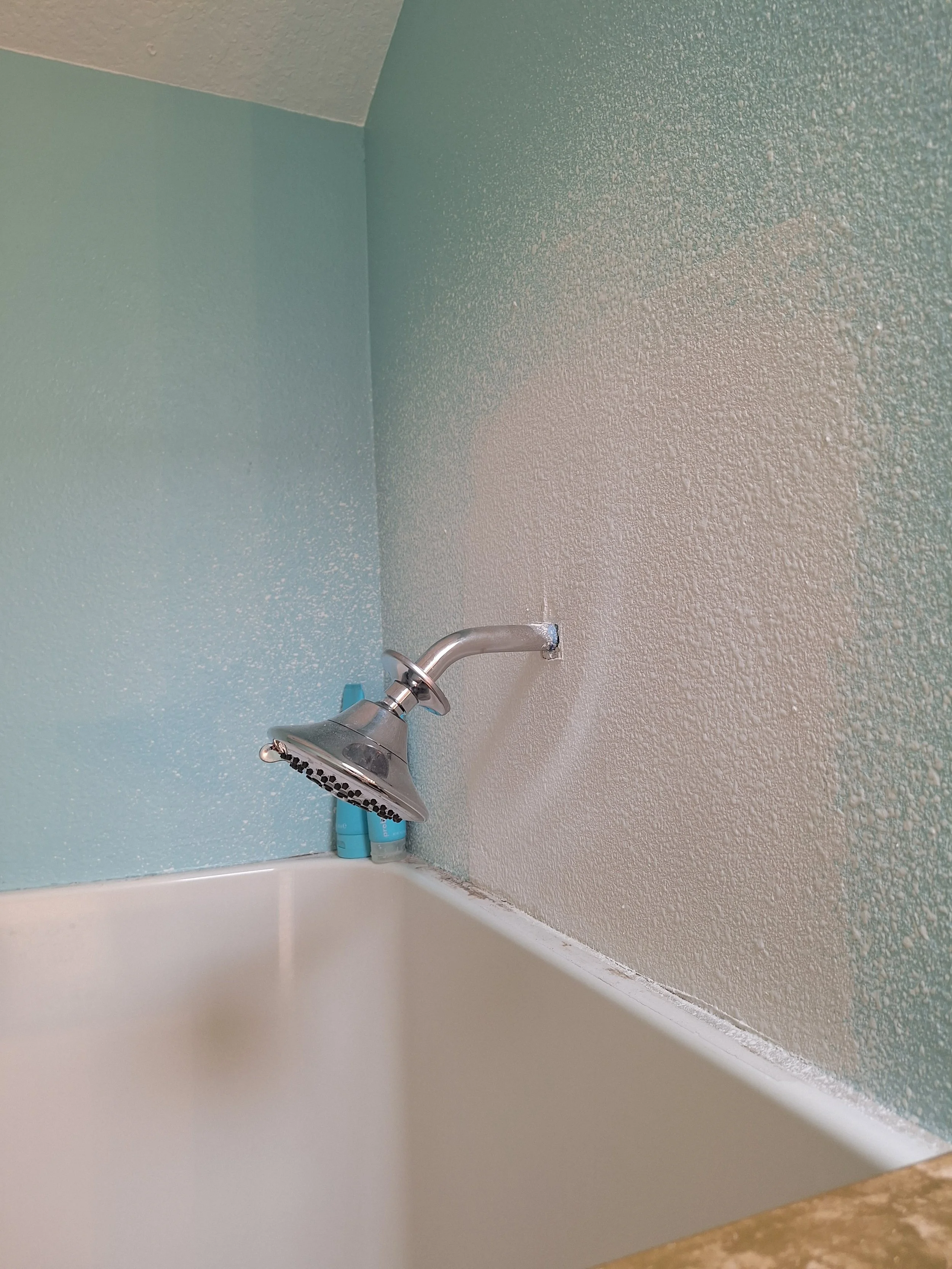 Close-up of a kitchen sink with a silver faucet attached to a textured two-tone wall, with a small section of countertop visible in the foreground.