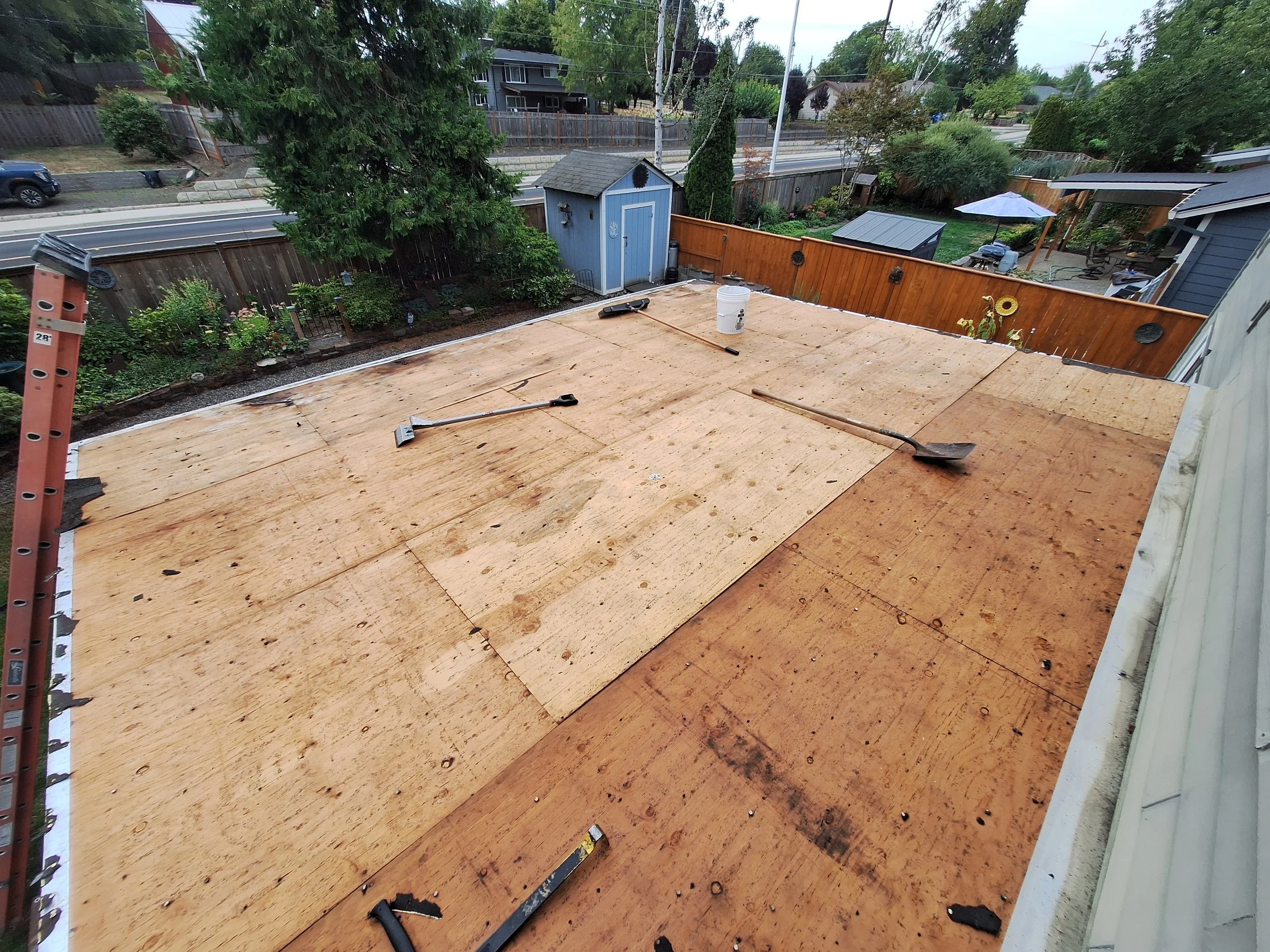 A rooftop under construction with wooden sheathing, roofing tools, and a salted lake in the background.