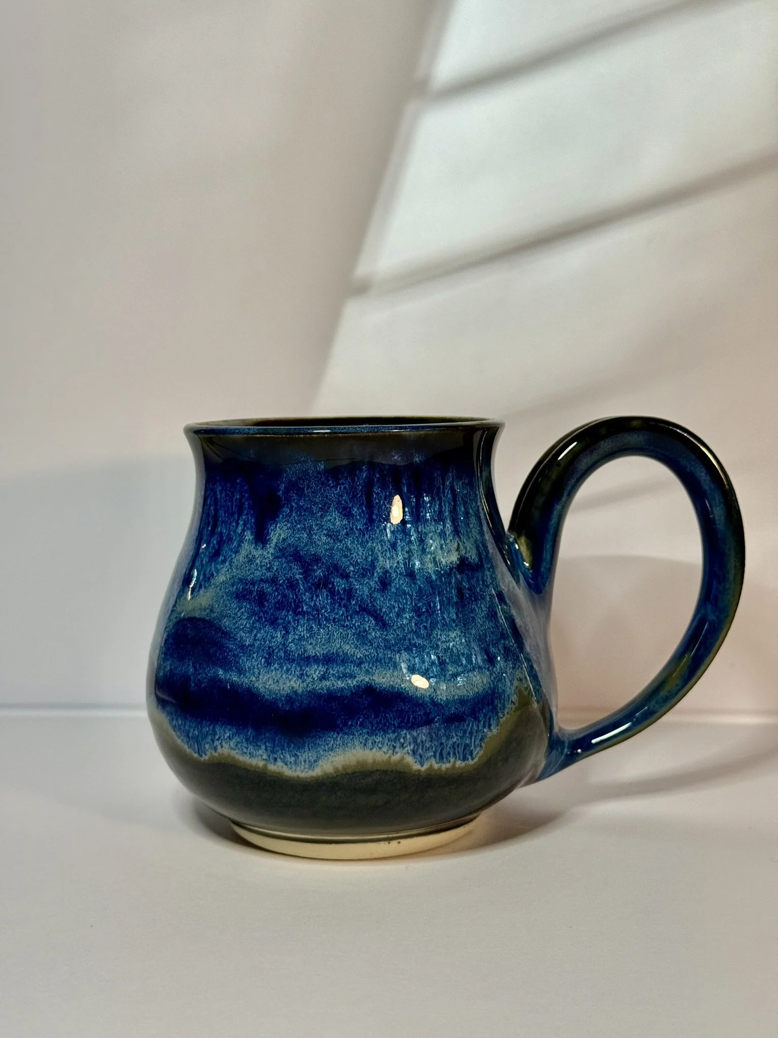 A ceramic mug with a blue glaze and a rounded shape, placed on a white surface against a plain white background.