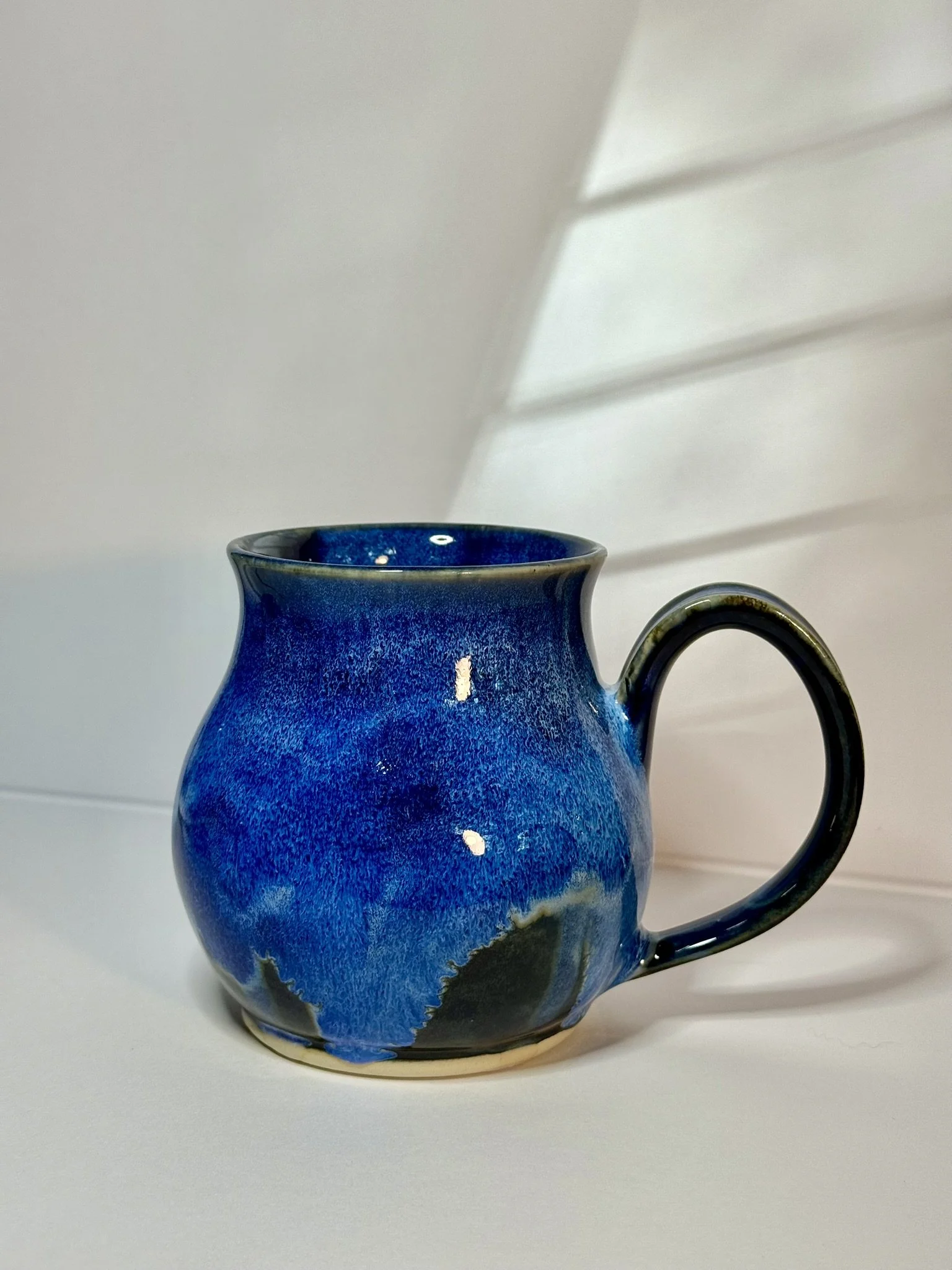 A ceramic mug with a blue glaze and black accents, placed on a white surface with a white background.