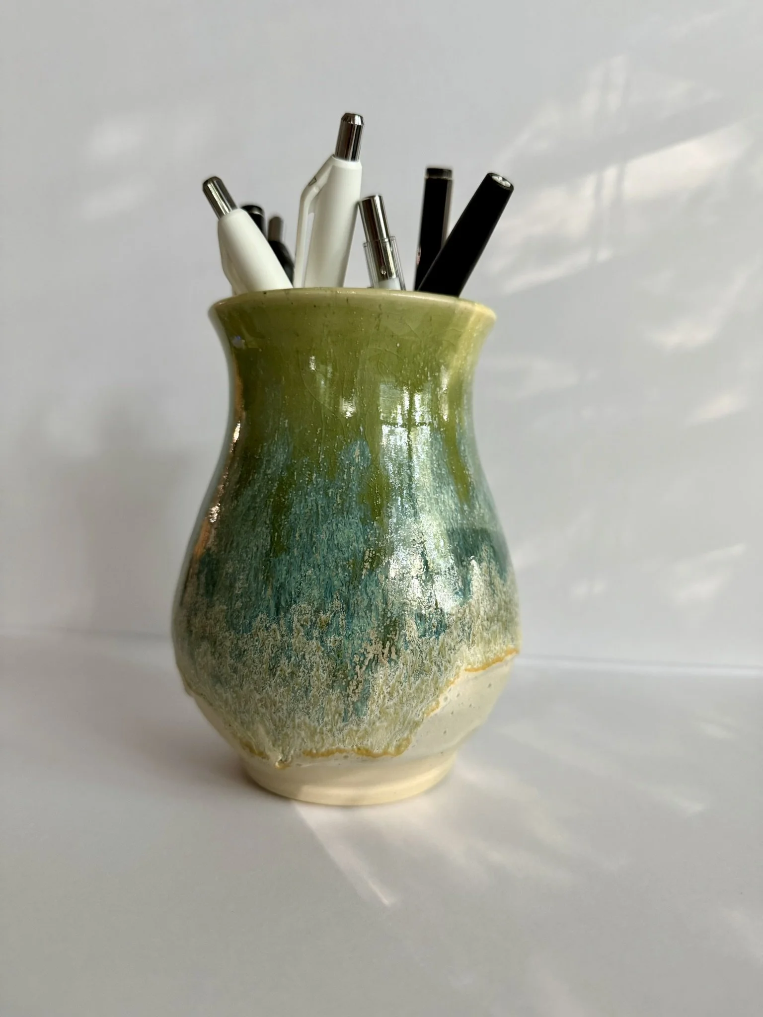 Ceramic vase holding black and white pens and markers on a light background.