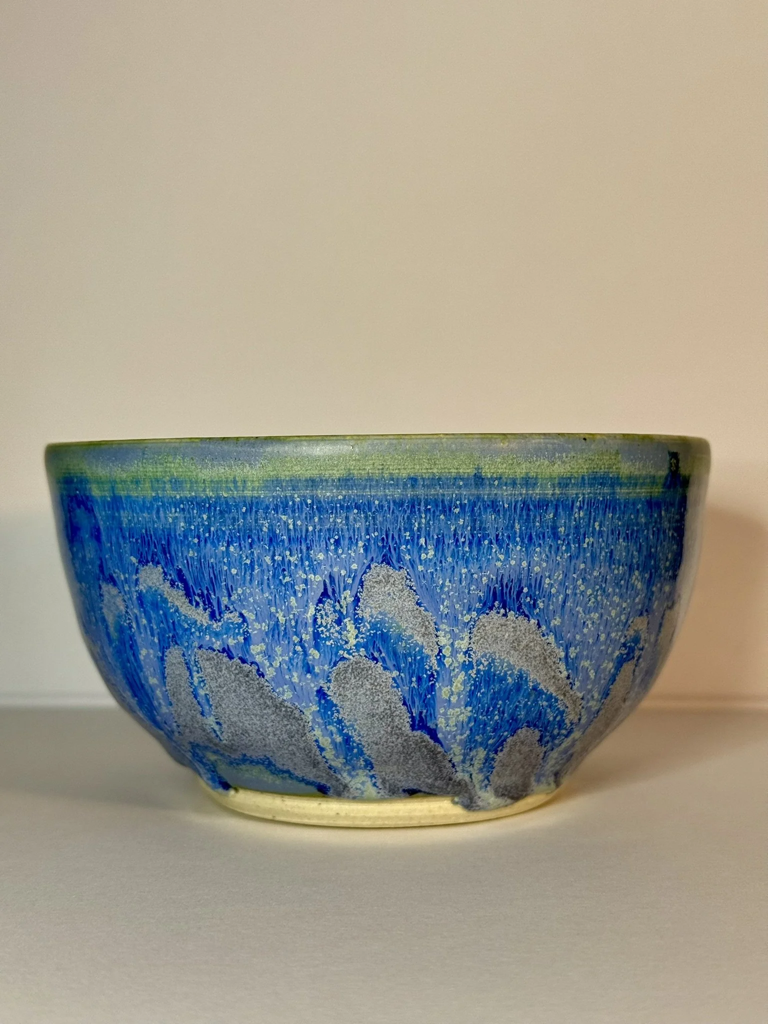 A ceramic bowl with a blue and gray floral pattern and a greenish rim, resting on a white surface against a beige background.