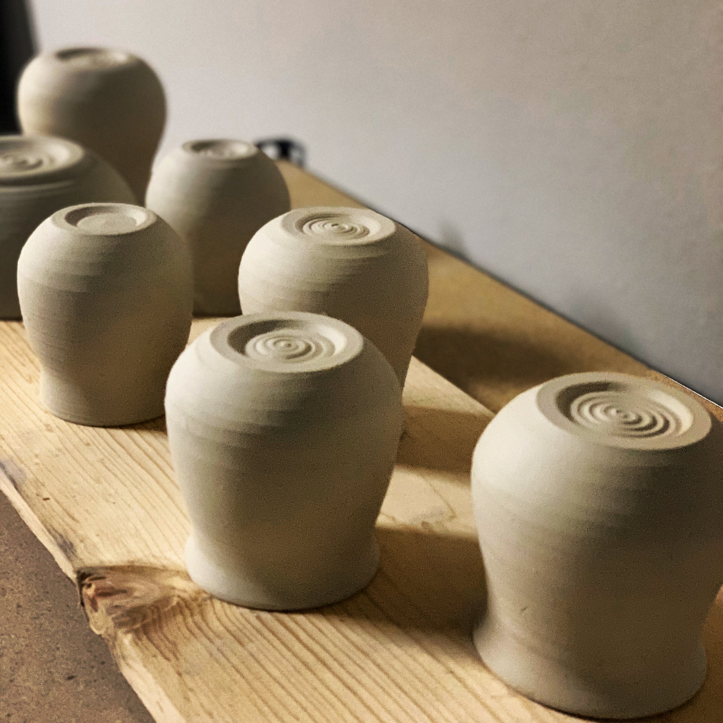 Multiple unglazed ceramic pots placed upside down on a wooden work surface, with some shadows falling on them.