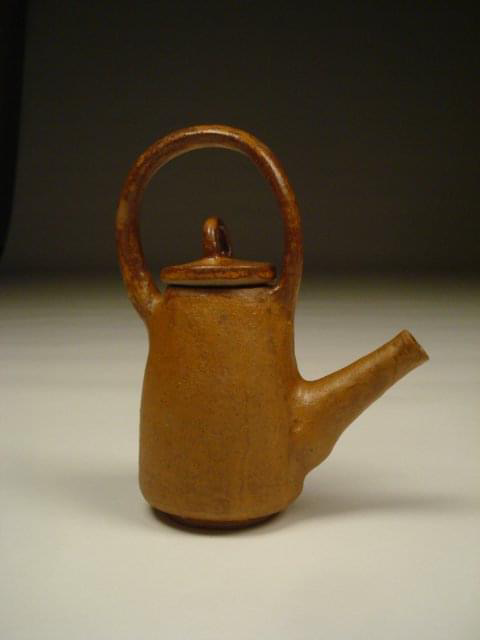 Small, brown clay teapot with a round handle and a short, stout spout.